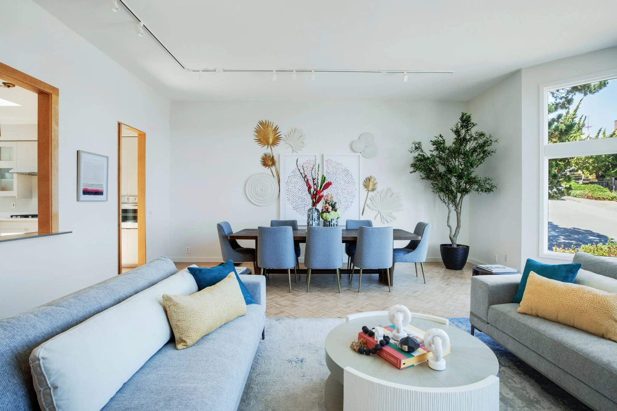 Spacious open-concept living area featuring contemporary grey sofas, a formal dining table for eight, and designer light-wood floors with custom inlays.