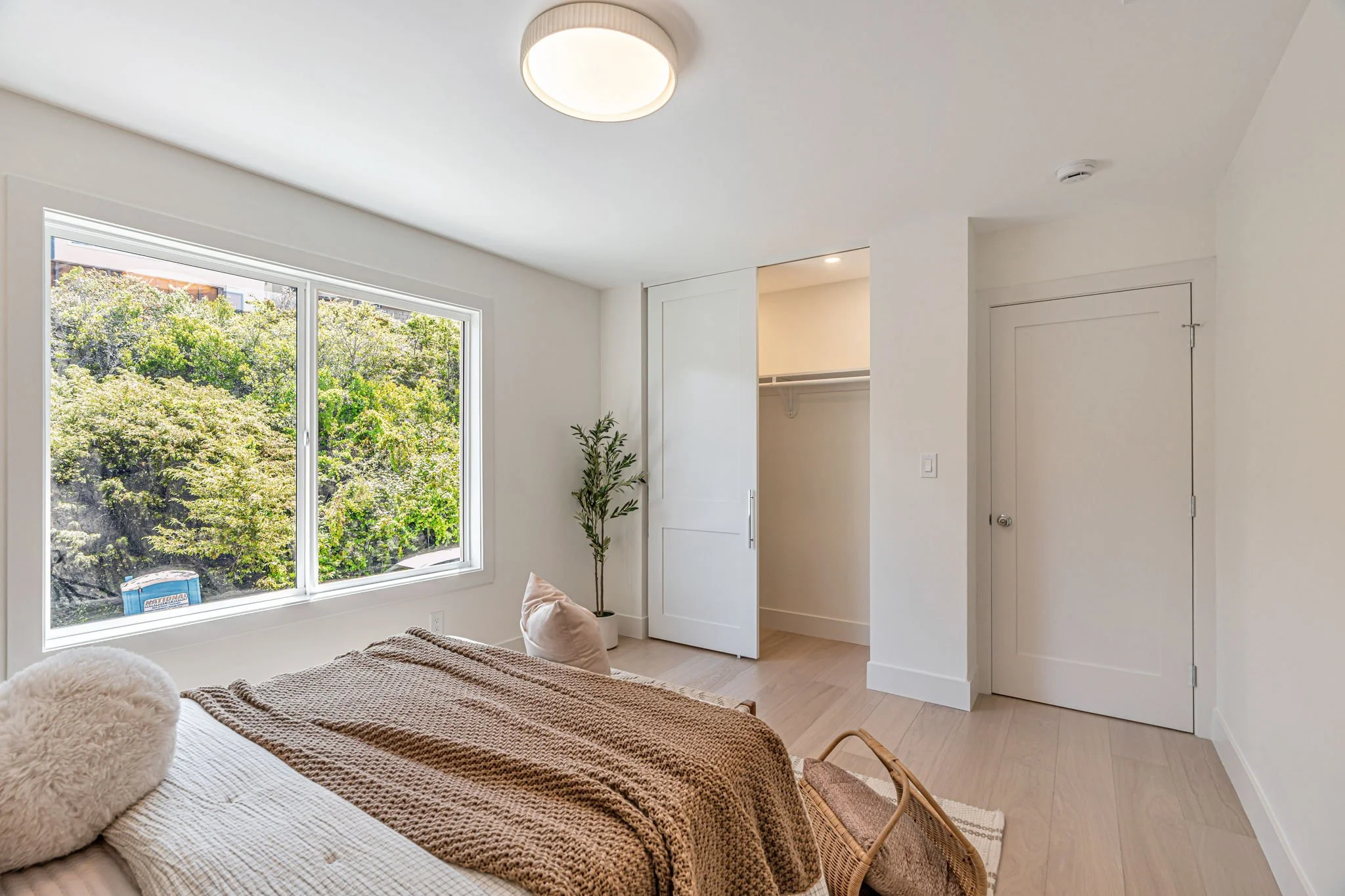 An alternate view of the second bedroom highlighting the large window and the clean lines of the architecture. The room features white walls, light wood flooring, and a sliding door closet.