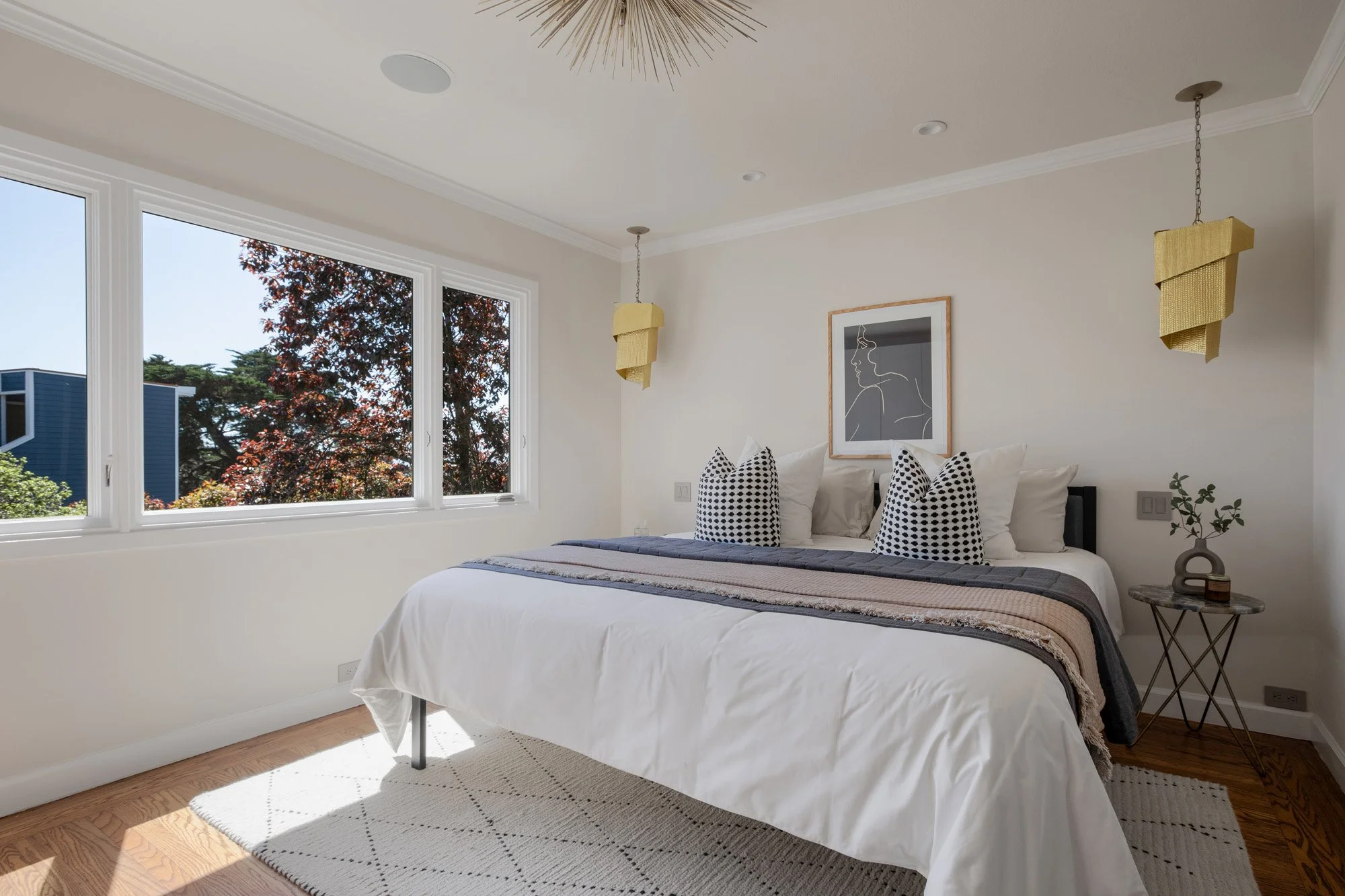 Sun-drenched primary bedroom with large windows, custom white wardrobes, and contemporary gold pendant lighting.