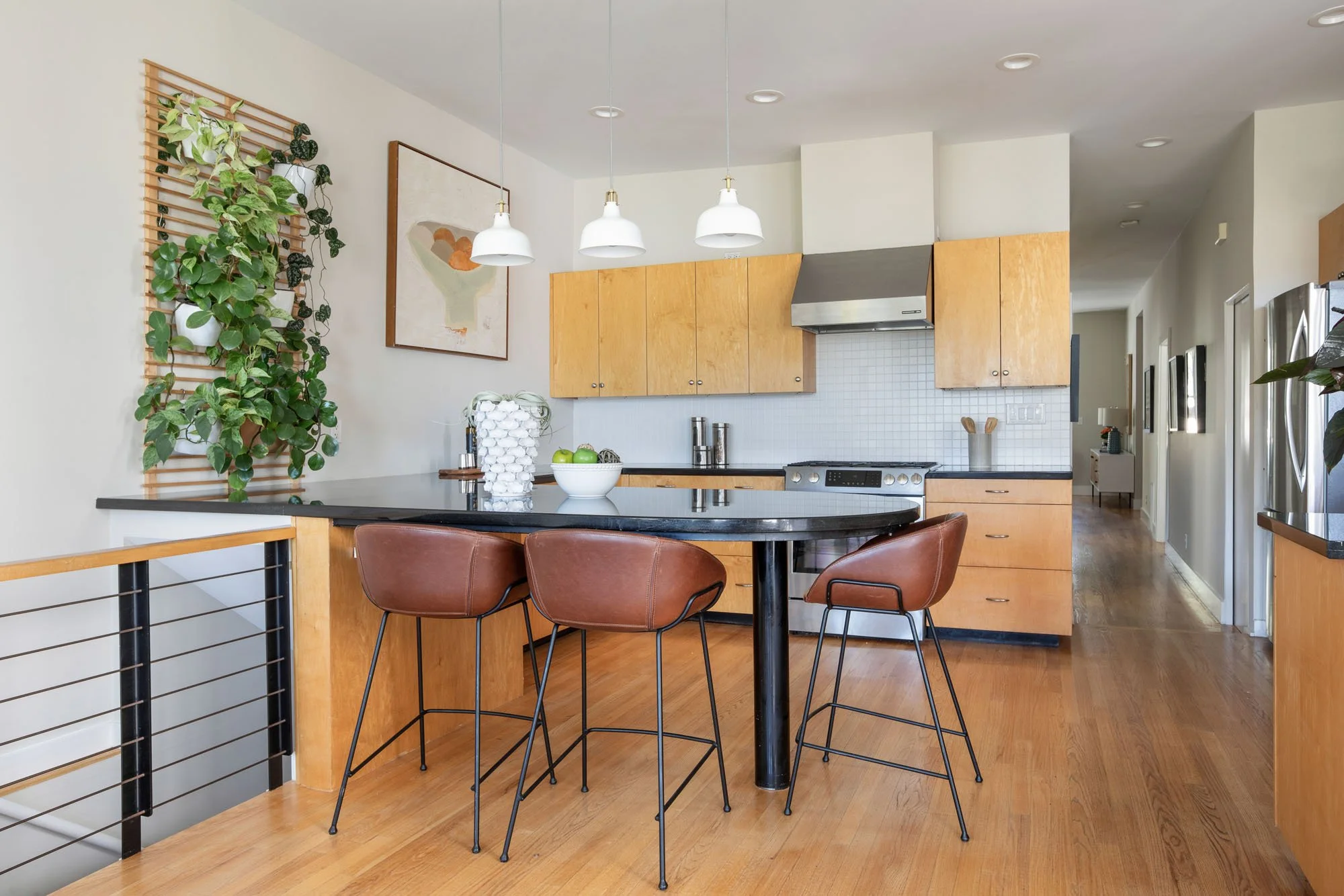 Contemporary kitchen with light wood cabinetry, black countertops, leather barstools at a peninsula, and a creative vertical herb garden wall.