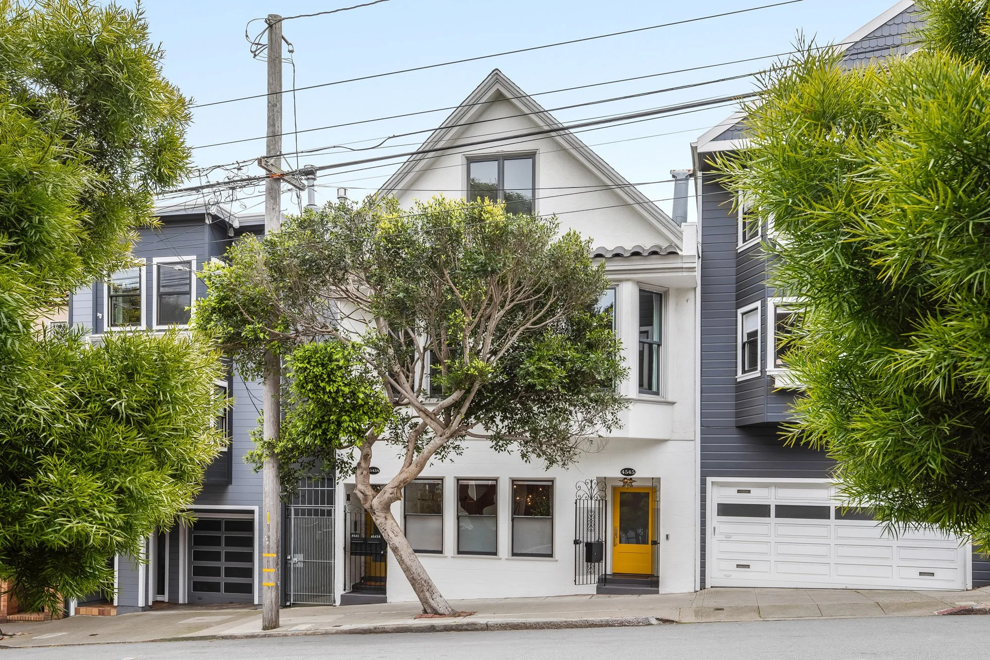 Exterior facade of luxury TIC at 4545 18th Street San Francisco — white stucco Victorian building with bold yellow front door, ornate iron security gate, and mature street tree in the Castro neighborhood