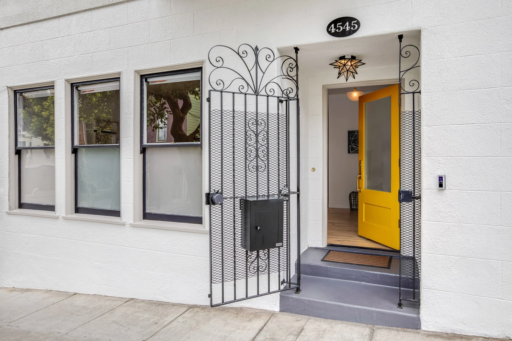 Close-up of 4545 18th Street San Francisco entrance featuring decorative wrought iron gate with scrollwork, star pendant light fixture, and vibrant yellow front door with hardwood flooring visible beyond