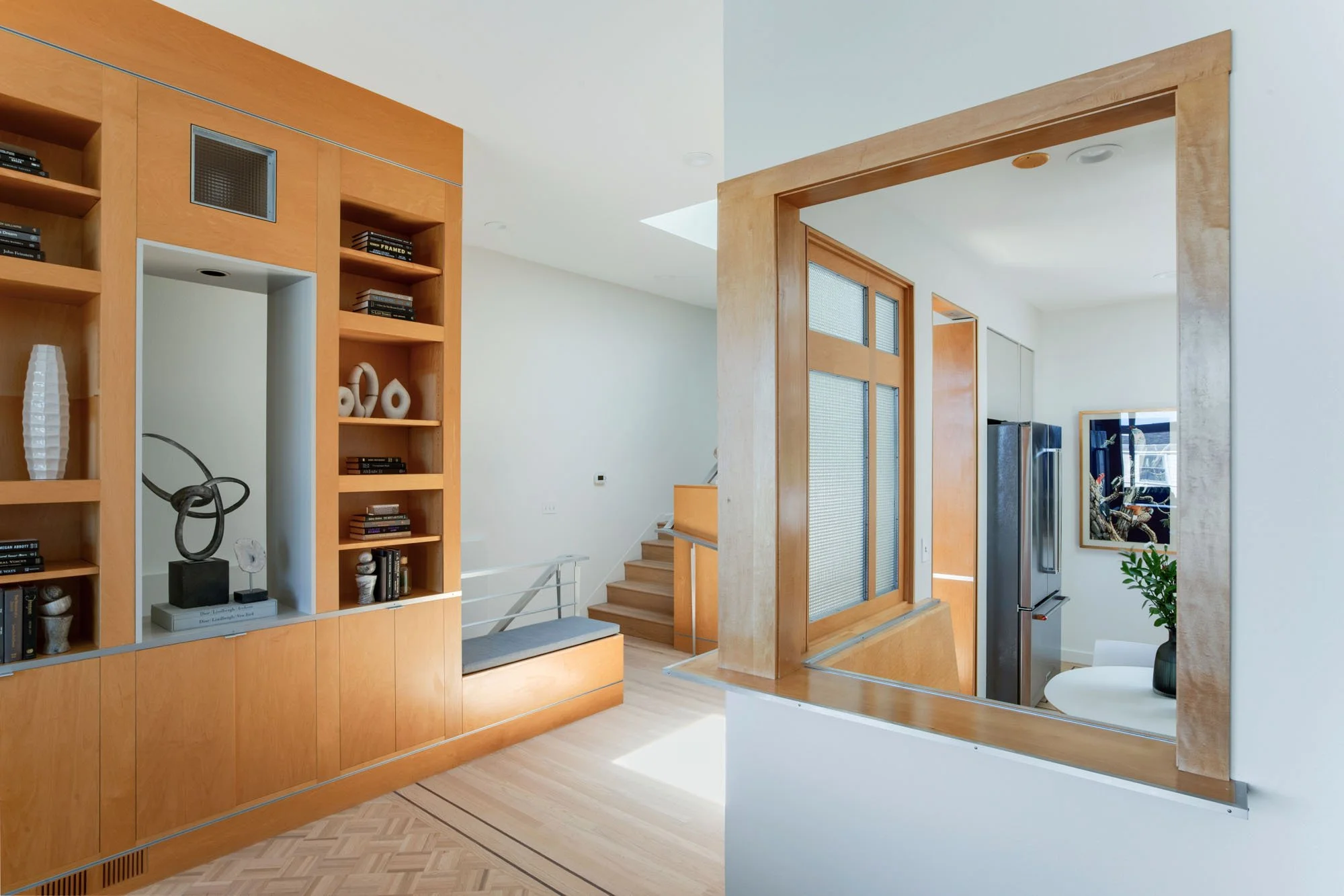 Architectural detail of a San Francisco luxury home showing custom floor-to-ceiling wood bookshelves, a built-in window seat, and a pass-through into the modern kitchen.
