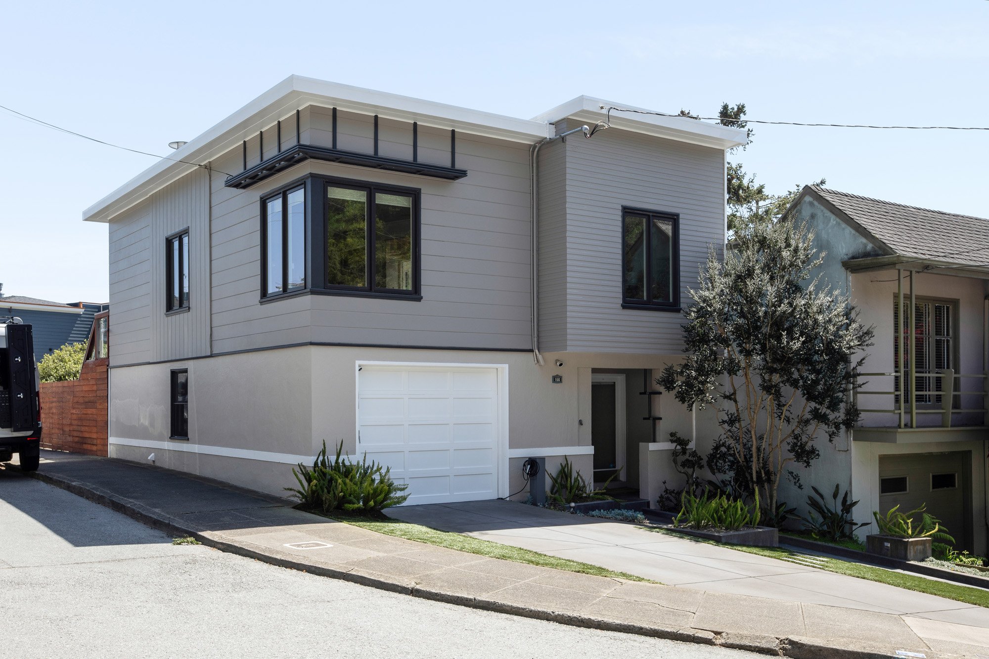 Contemporary two-story home exterior with a white garage door, neutral gray siding, and a clean, modern architectural silhouette.