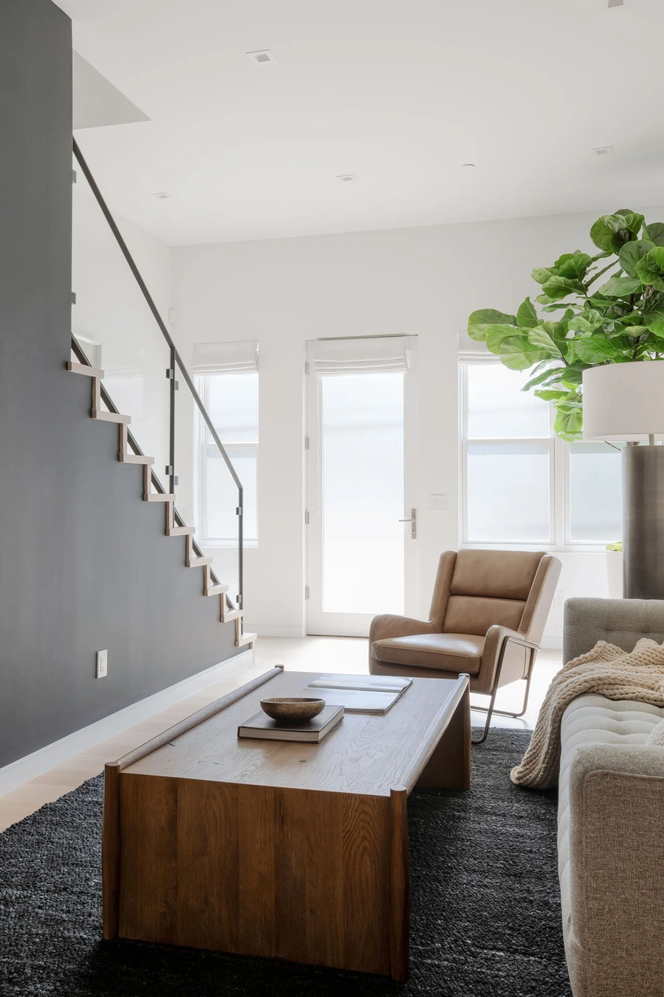 Contemporary living space at 290 Day Street 
showcasing a tan leather armchair, solid oak coffee table, and a glass-paneled architectural staircase.