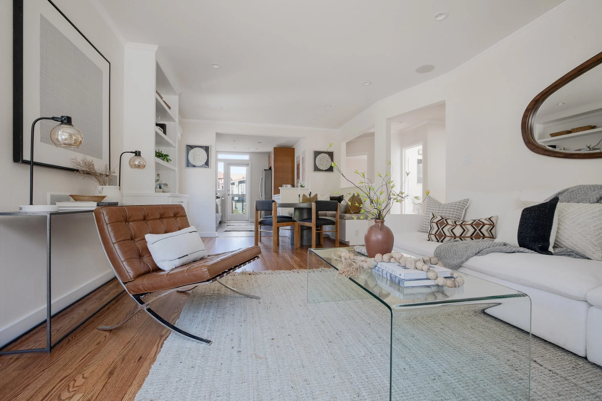 Wide view of a modern living room featuring a glass coffee table, brown leather chair, and a white sectional sofa.