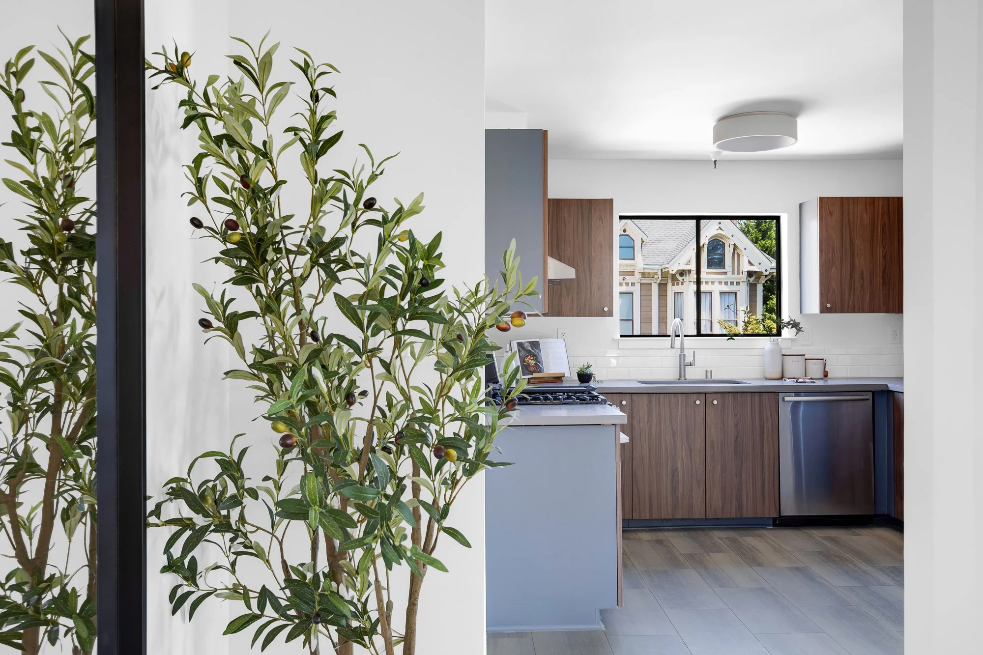 View into the renovated kitchen at 932 Broderick Street #2 showing walnut cabinetry, stainless appliances, and a Victorian rooftop view through the window.