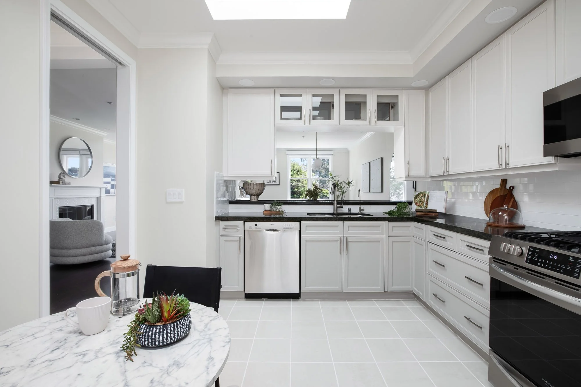 Bright kitchen at 2172 Fell Street San Francisco with skylight, white shaker cabinets, dark granite countertops, stainless steel dishwasher, gas range, subway tile backsplash, and marble breakfast table with garden window view