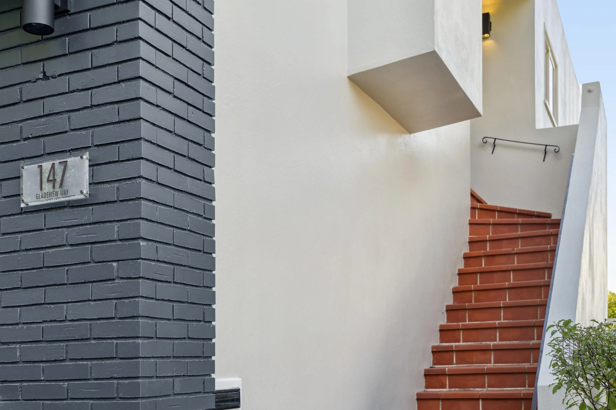 Close-up of the address plaque for 147 Gladeview Way mounted on a dark grey brick wall next to a terracotta outdoor staircase.