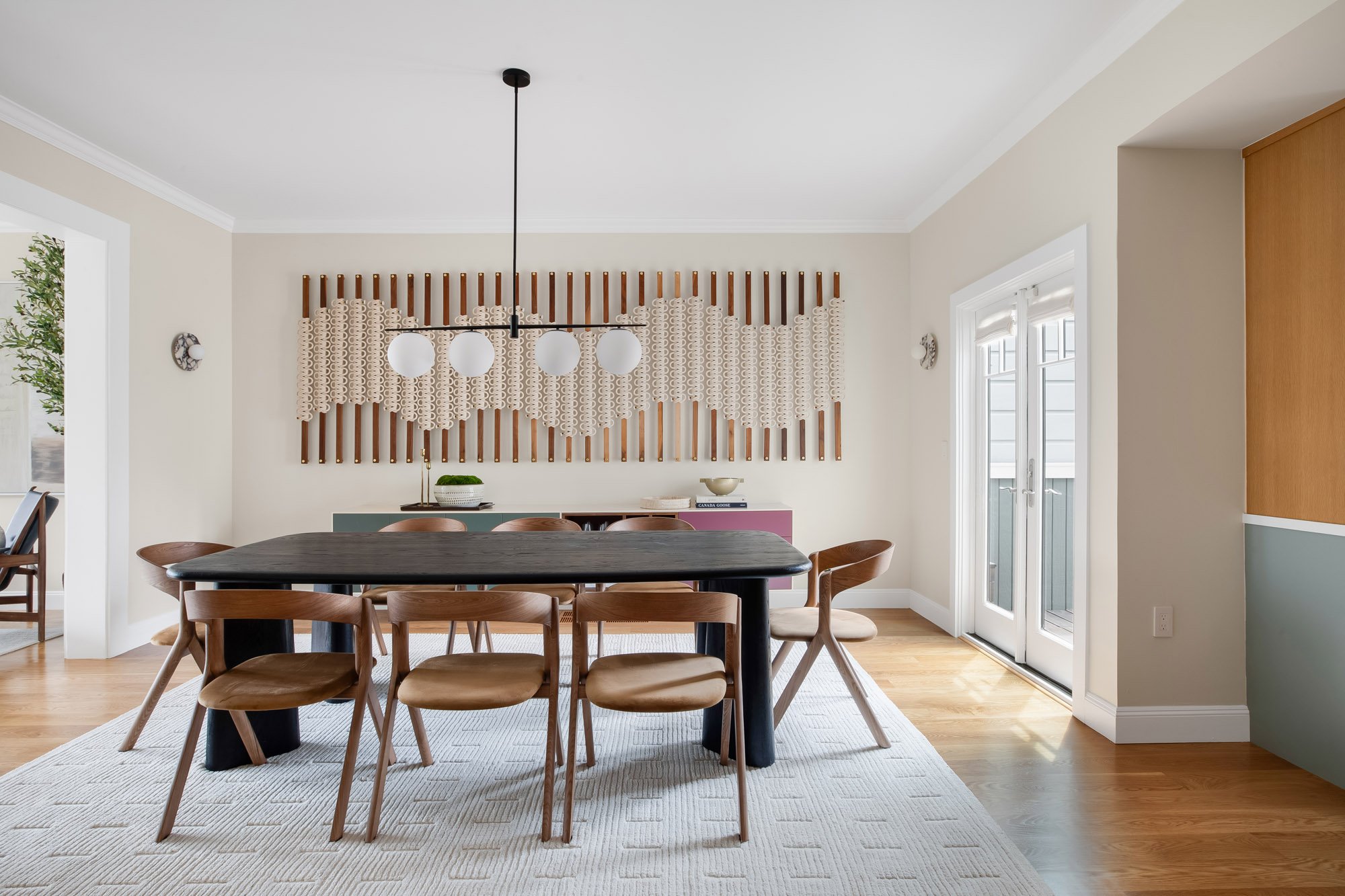 Dining room at 771 Elizabeth Street in Noe Valley featuring a wall-anchored Windy Chien "Hitching Post" art installation, globe pendant chandelier, black oak table, and French doors to a balcony. 