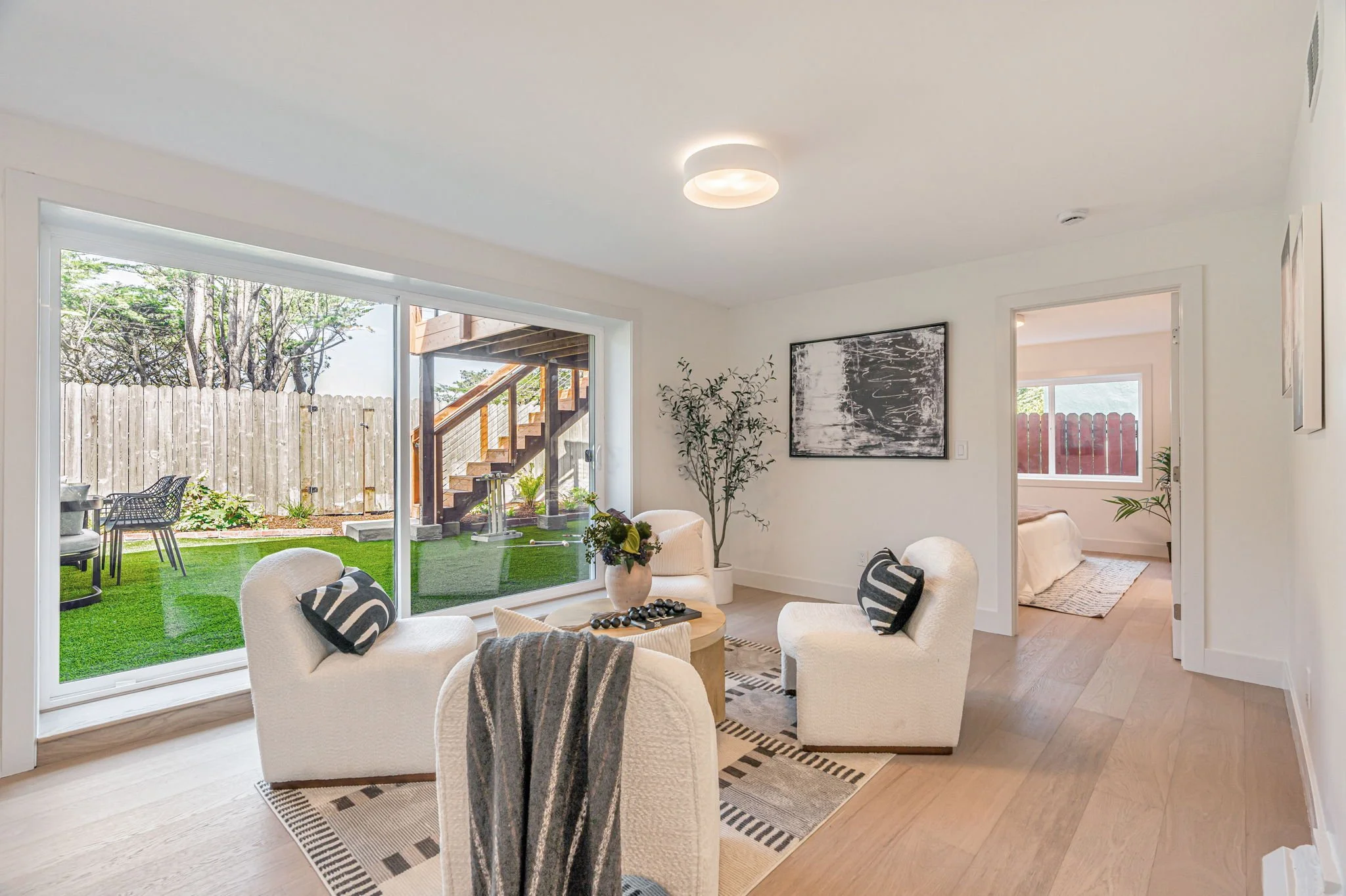 Bright media room with white bouclé chairs, a round wood coffee table, and a large sliding glass door opening to a lush green San Francisco backyard.