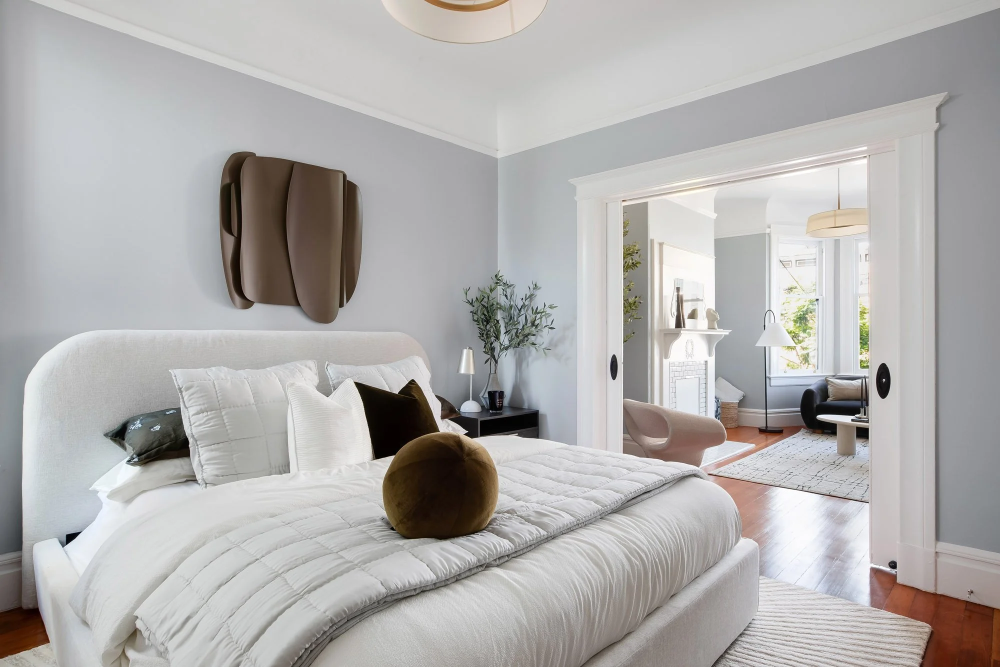 Guest bedroom with upholstered bed and wall art, pocket doors open to the living room beyond