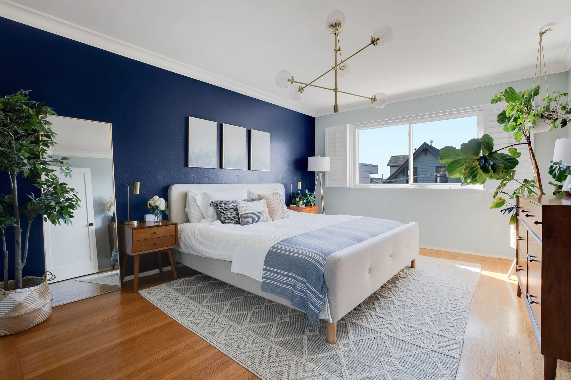 Modern primary bedroom at 144 Lower Terrace featuring a deep navy blue accent wall, mid-century modern wood nightstands, and a gold sputnik chandelier.
