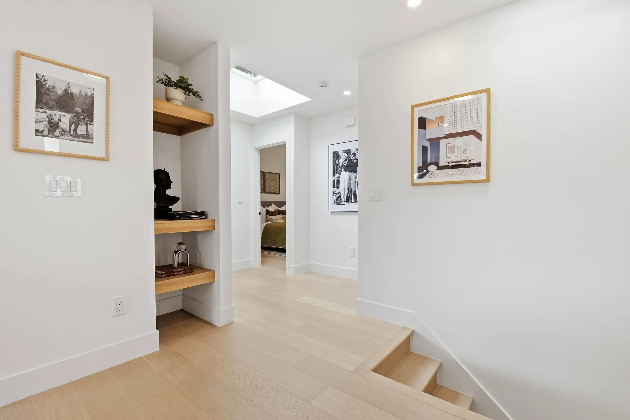 Bright, minimalist hallway in a renovated SF home featuring light oak floors, built-in display shelving, and natural light from a skylight.