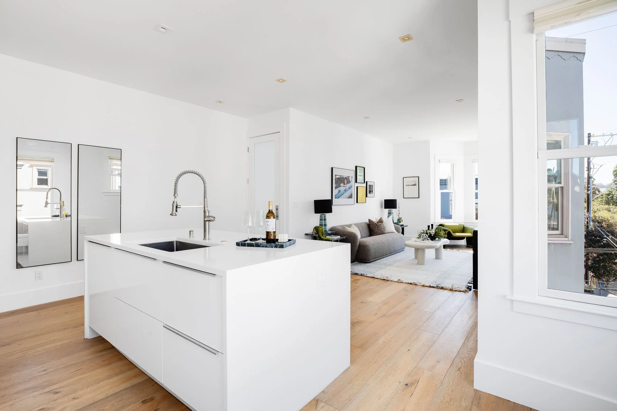 Wide view of a modern Mission District luxury condo showing the white kitchen island and open-concept living area.