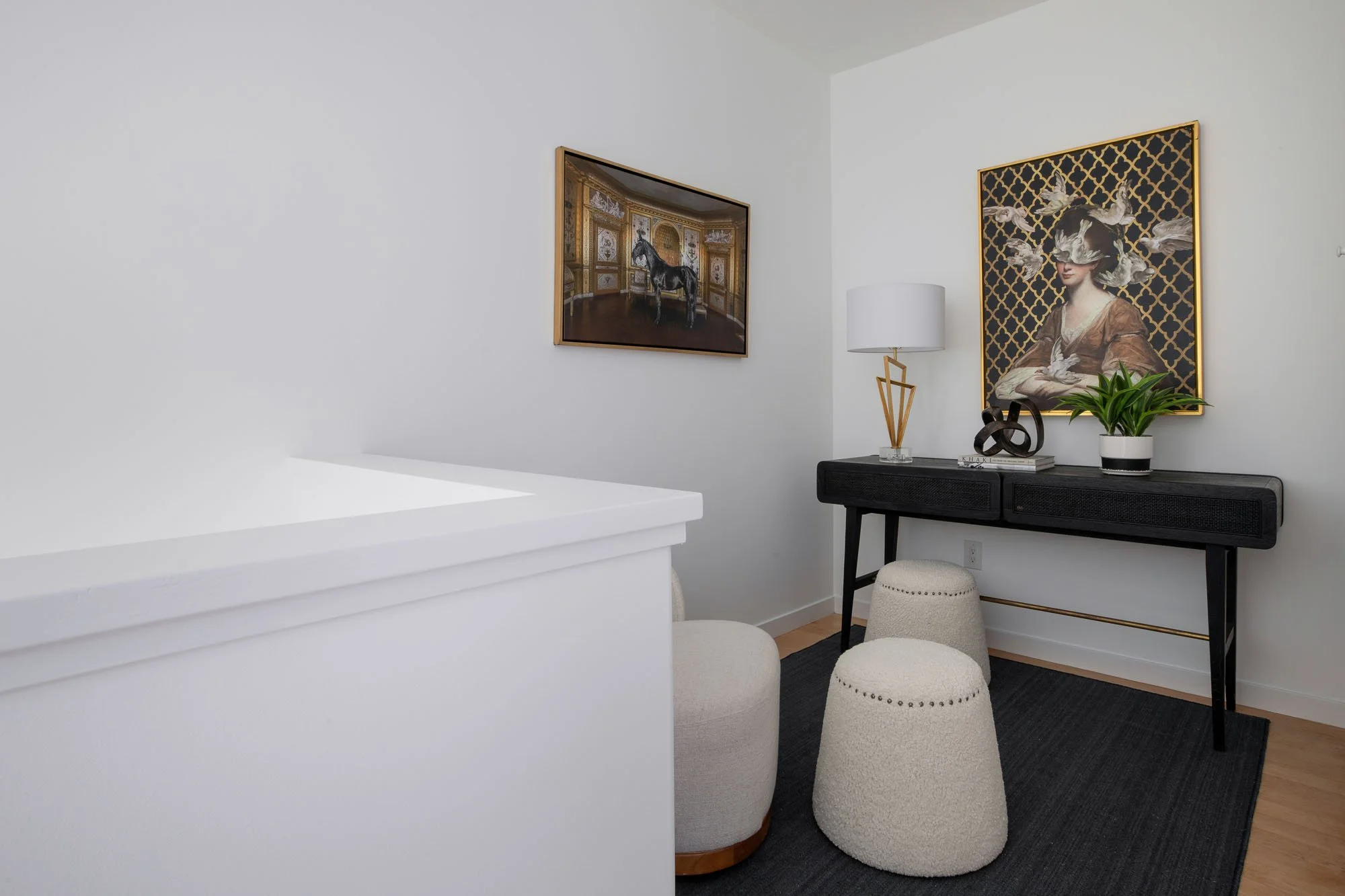 A stylish landing area or small home office featuring a black wood console desk, white boucle ottomans, and curated gold-framed wall art.