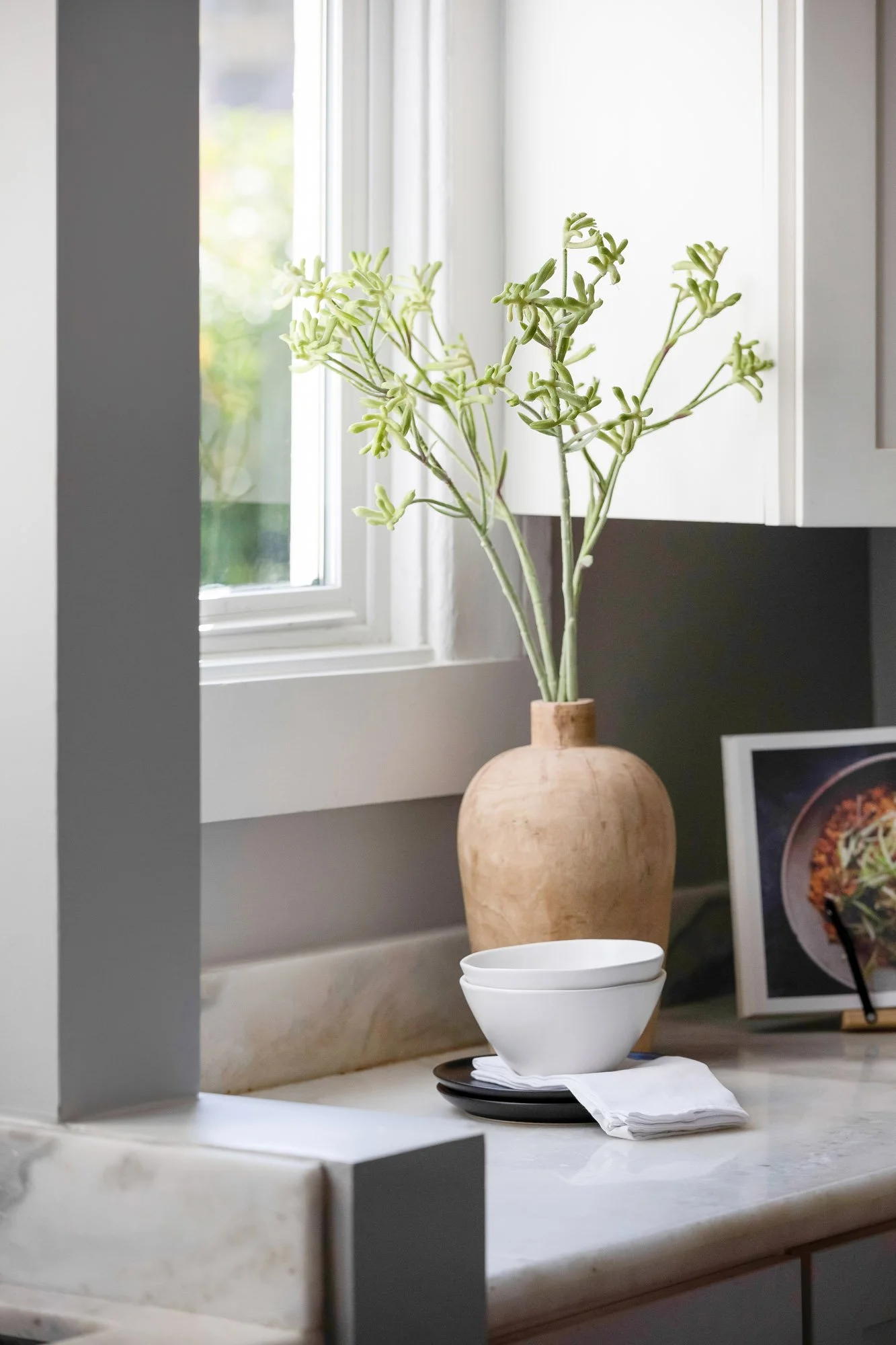 Kitchen window nook with a vase, ceramic bowls, and open corner shelving