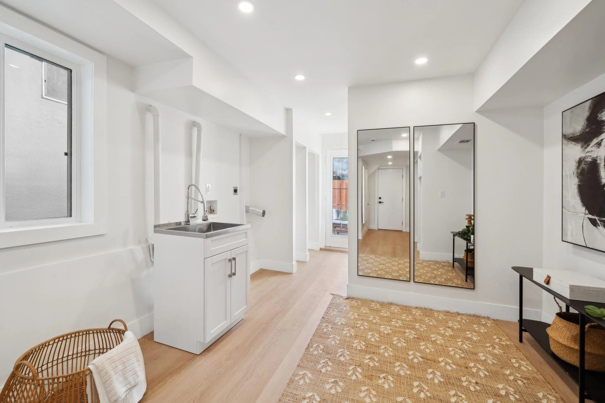Clean, white laundry or mudroom area with a utility sink, large floor-to-ceiling mirrors, and durable light wood-look flooring.