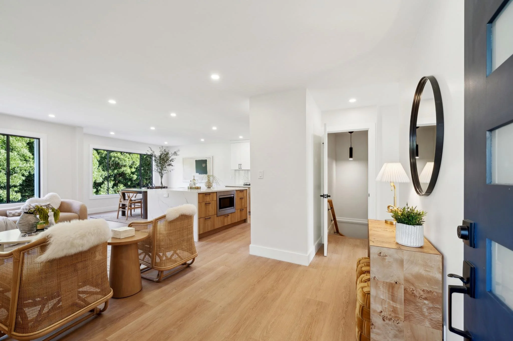 Bright, open-concept interior featuring light hardwood floors, a modern kitchen with a waterfall island, and an entryway with a circular black mirror and designer furniture.
