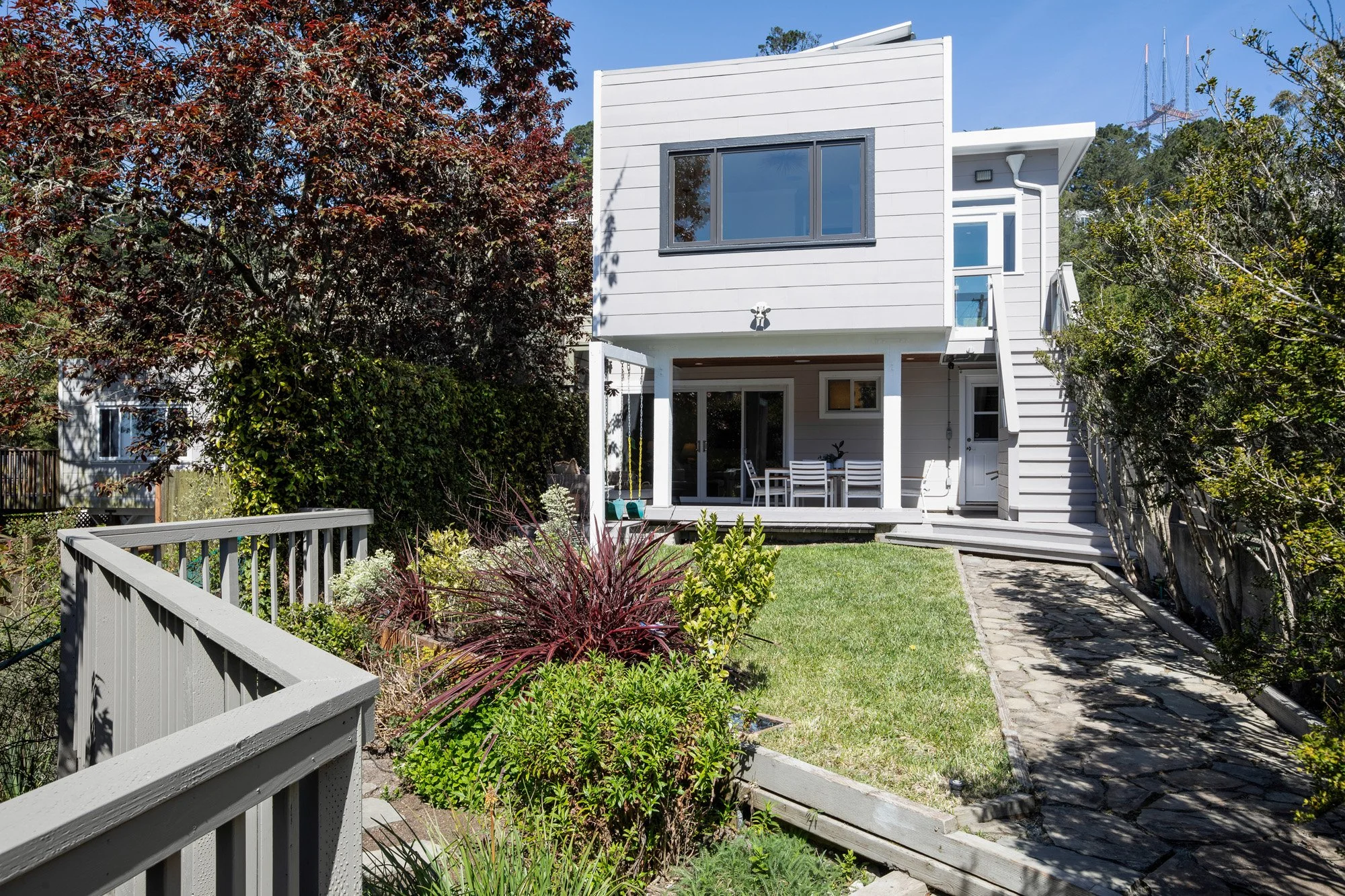 Contemporary two-story home exterior featuring a manicured lawn, stone pathway, and a private upper-level balcony.