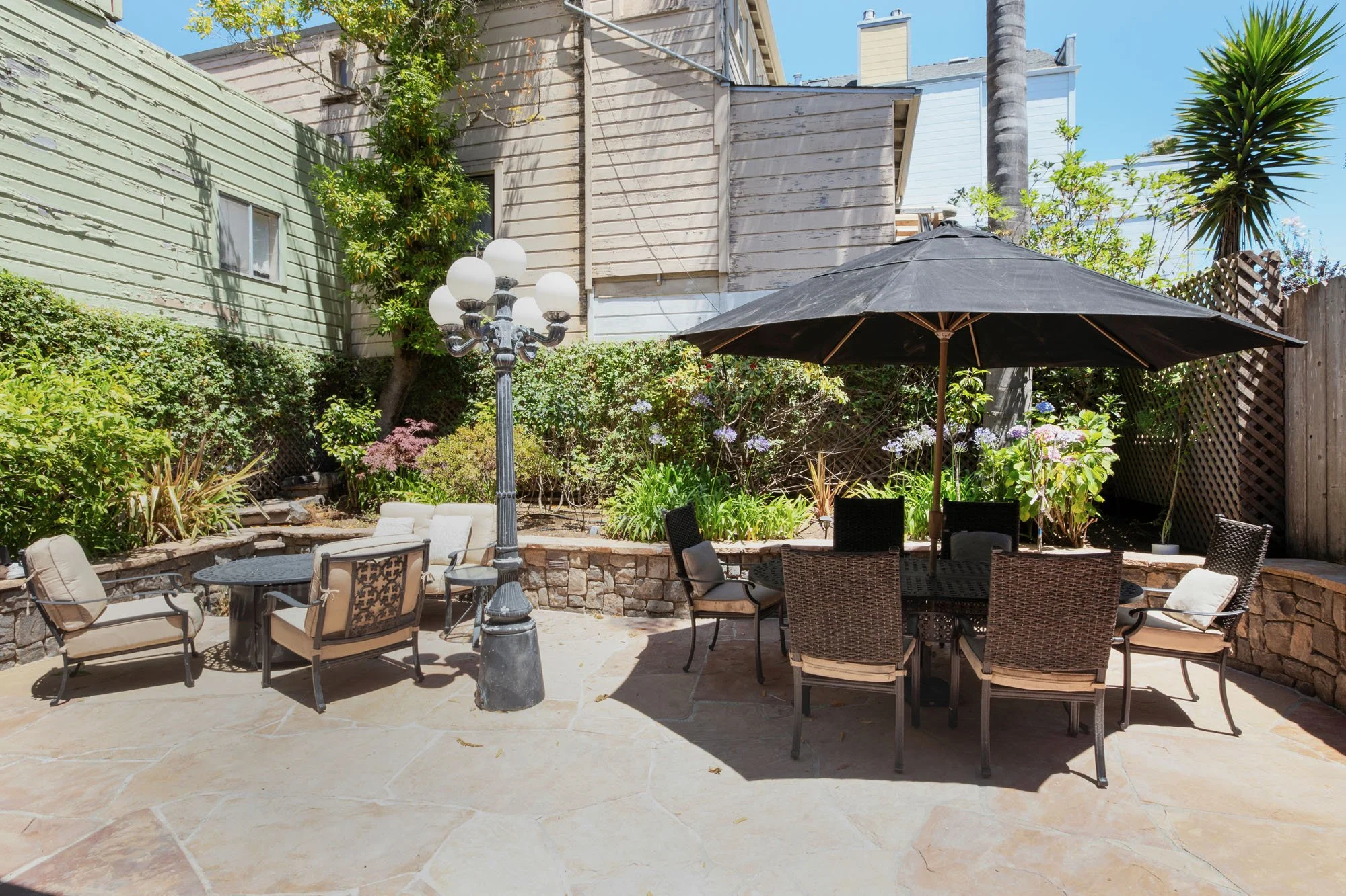 Landscaped backyard retreat featuring a stone retaining wall, lush greenery, and comfortable outdoor lounge furniture for entertaining.