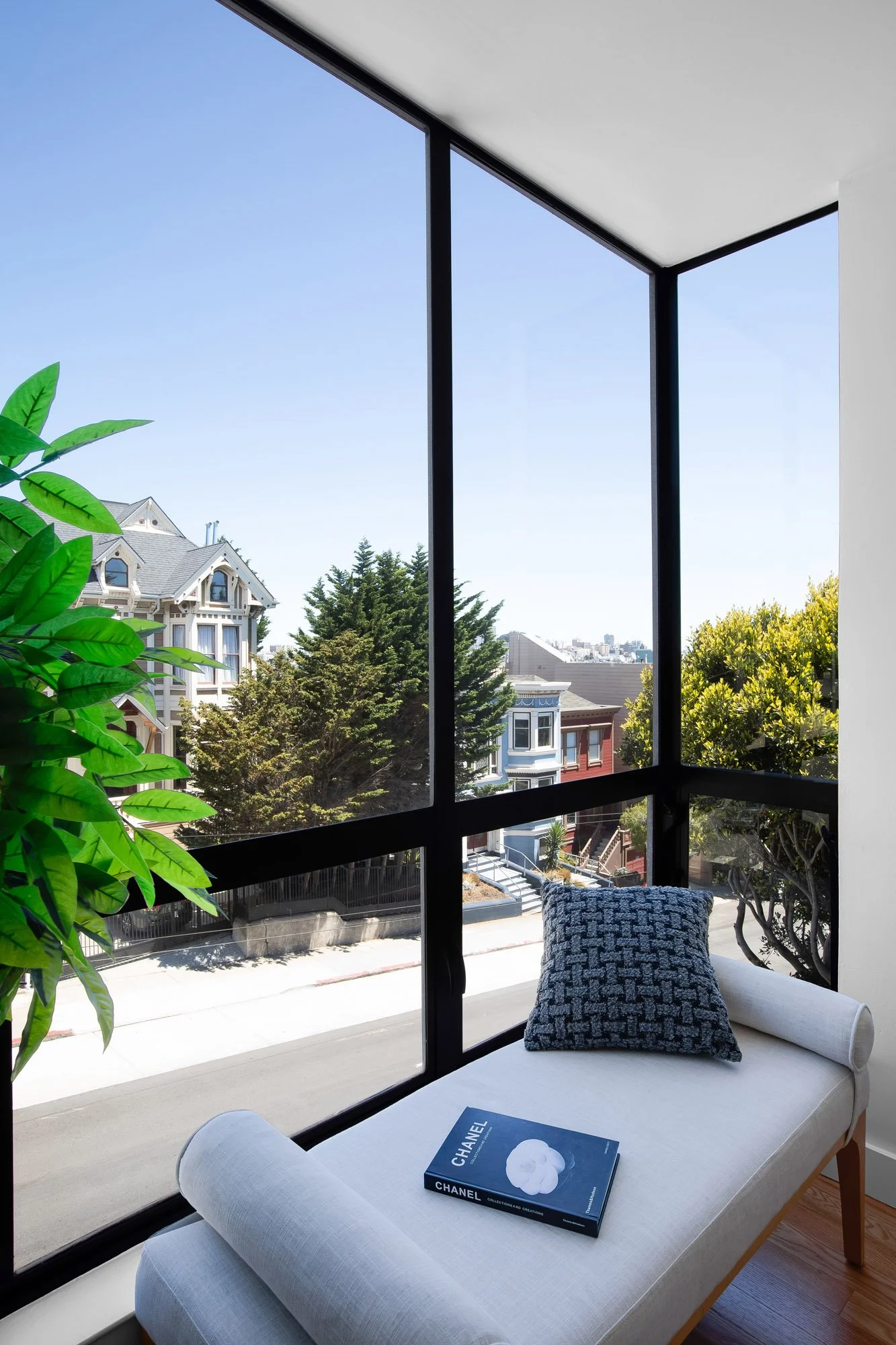 Floor-to-ceiling corner windows with a window-seat daybed at 932 Broderick Street #2, framing San Francisco Victorian rooftops and a peek of the downtown skyline.