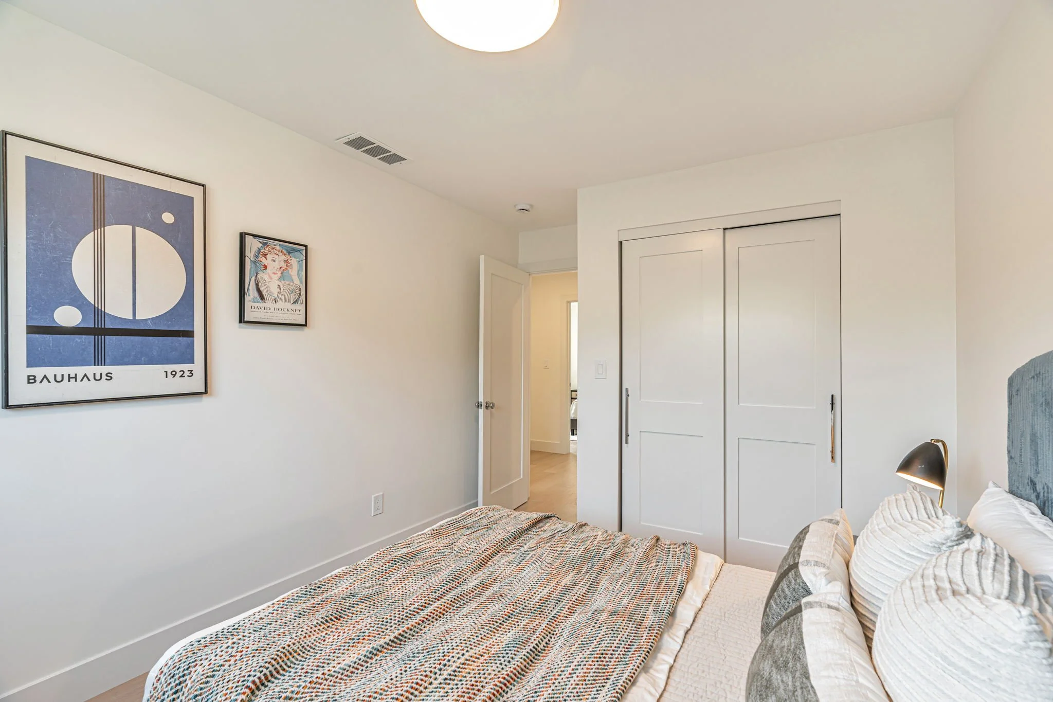 Modern San Francisco bedroom interior featuring neutral white walls, light hardwood floors, a Bauhaus art print, and white sliding closet doors.