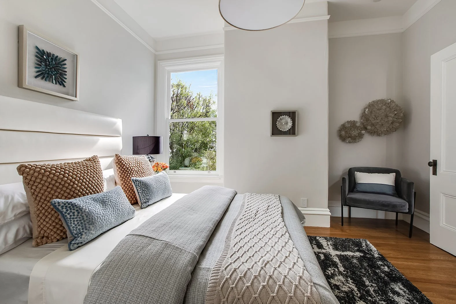 Bright guest bedroom featuring an upholstered headboard, designer textures, and large windows overlooking lush Pacific Heights greenery.