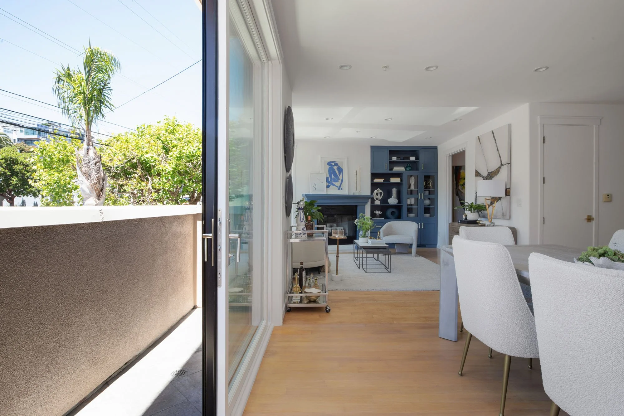 Bright, modern living room with large sliding glass balcony doors showcasing an indoor-outdoor flow, white walls, and slate blue accent cabinetry.