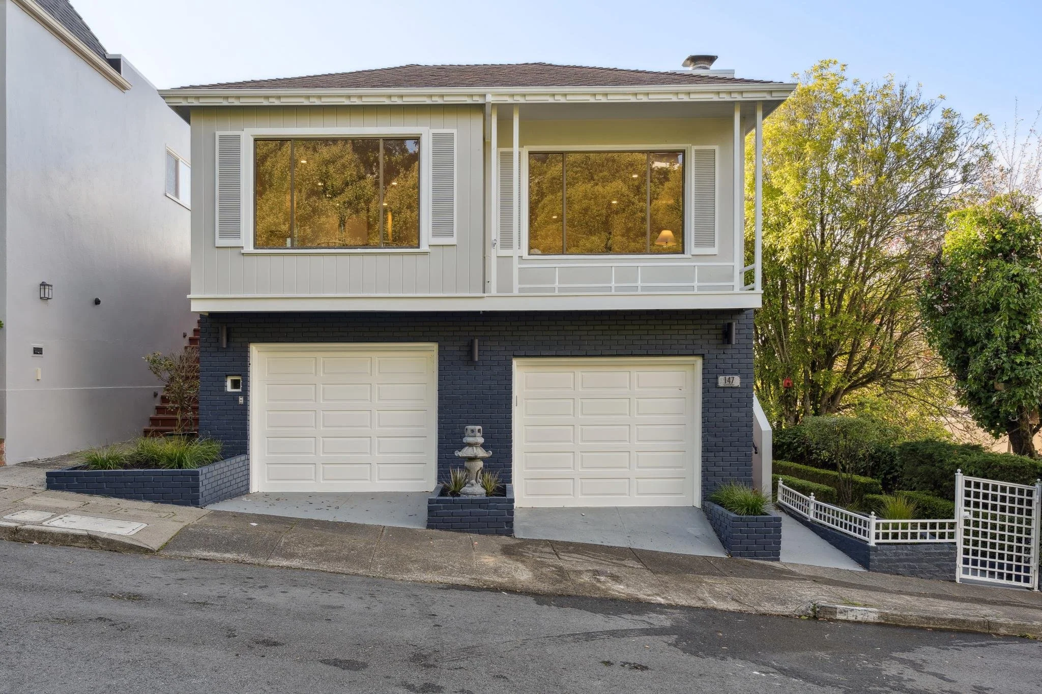 Front elevation of 147 Gladeview Way, a renovated San Francisco home on a sloped street, showcasing a dual-car garage, manicured planters, and a white terrace railing.