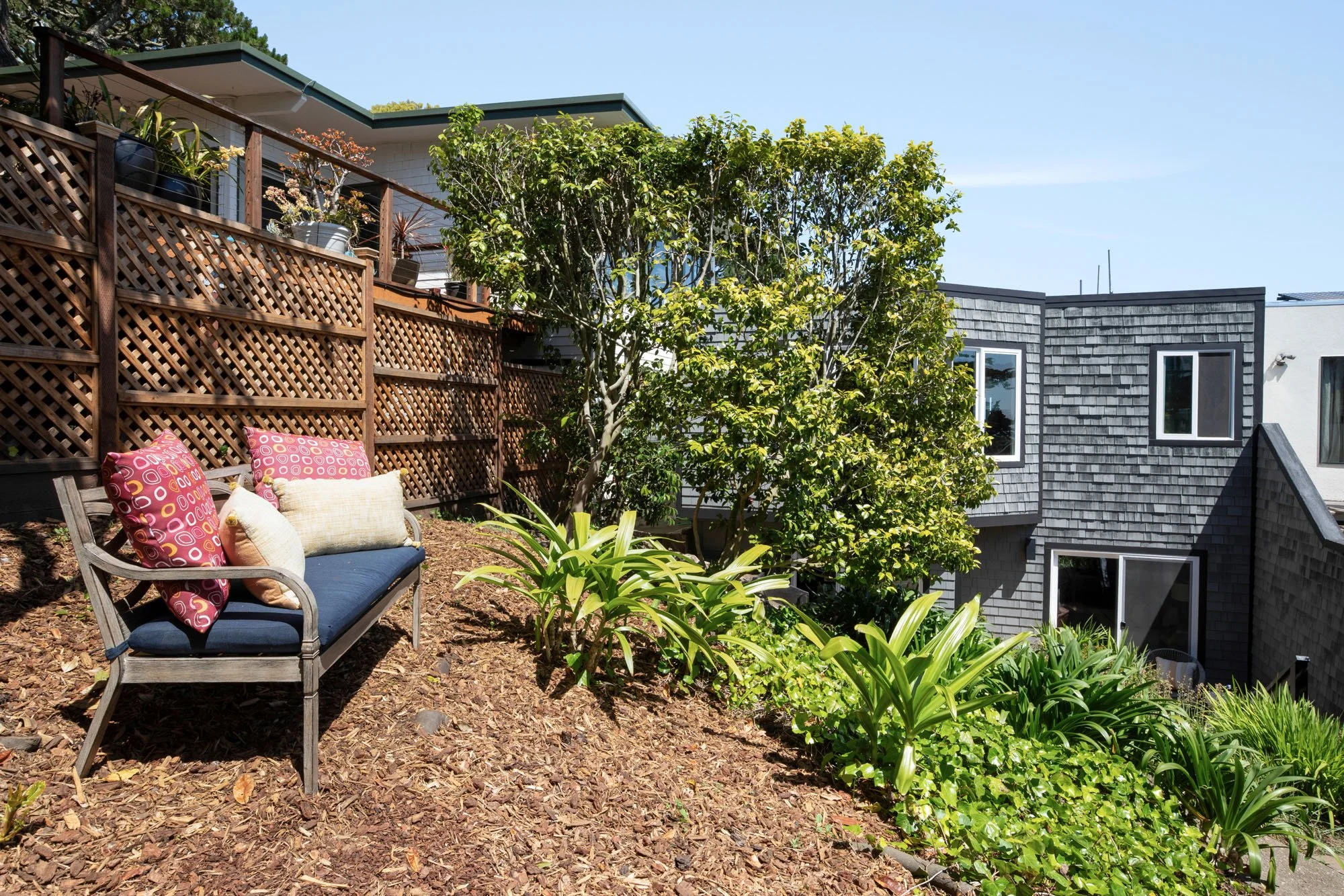 Tiered hillside backyard in San Francisco with professional drought-tolerant landscaping, a decorative wood lattice fence, and a quiet garden seating area.