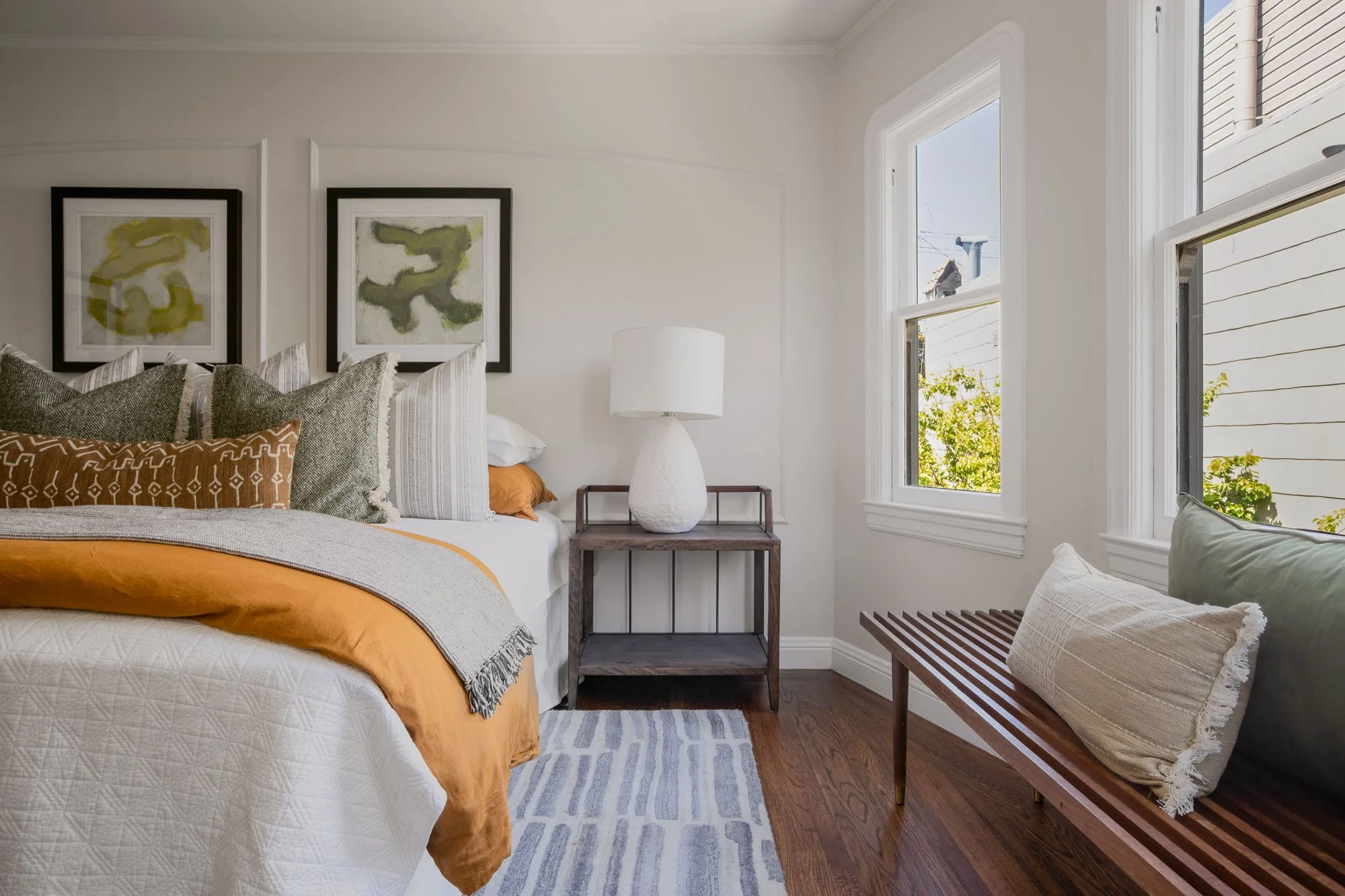 Detailed view of bedroom staging including a mid-century modern bench, textured linens, and designer bedside lighting.