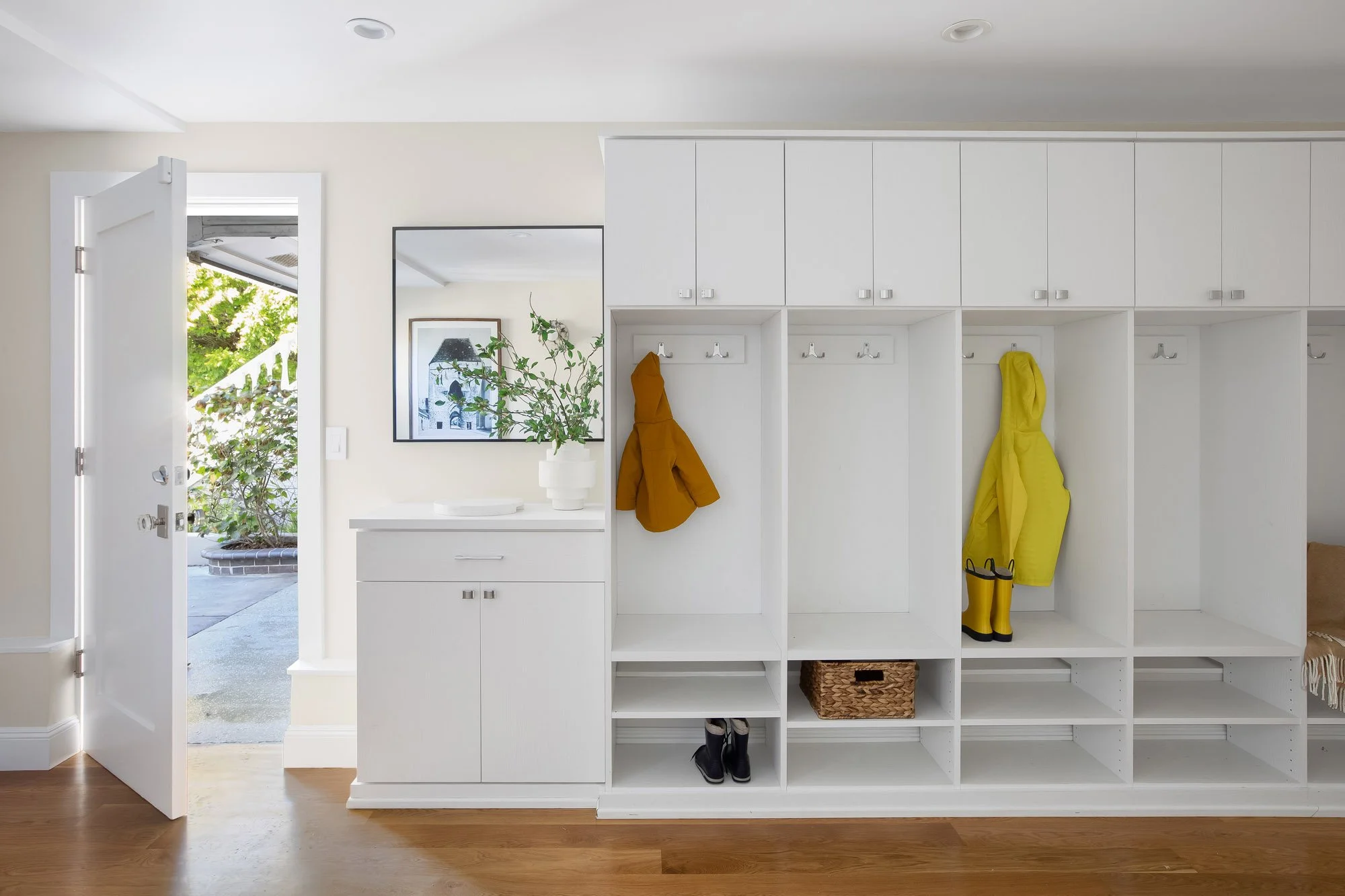 Custom mudroom at 771 Elizabeth Street with white built-in lockers, coat hooks, cubbies, and bench storage beside a door opening to the garage and driveway.