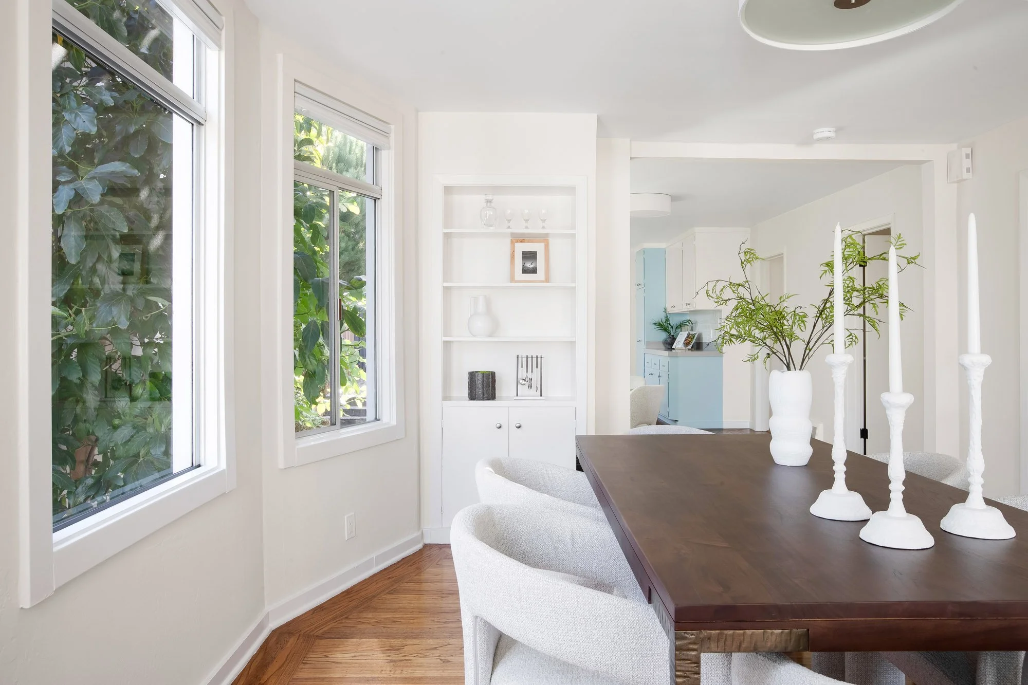 Built-in cabinet with open shelving beside garden-view windows in the dining area of an Upper Noe Valley home, with the kitchen beyond