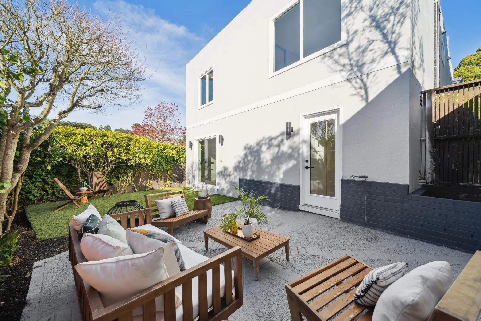 Outdoor entertaining space at 147 Gladeview Way, showing a modern grey stucco exterior, sliding glass doors, and a manicured garden area with mature trees.
