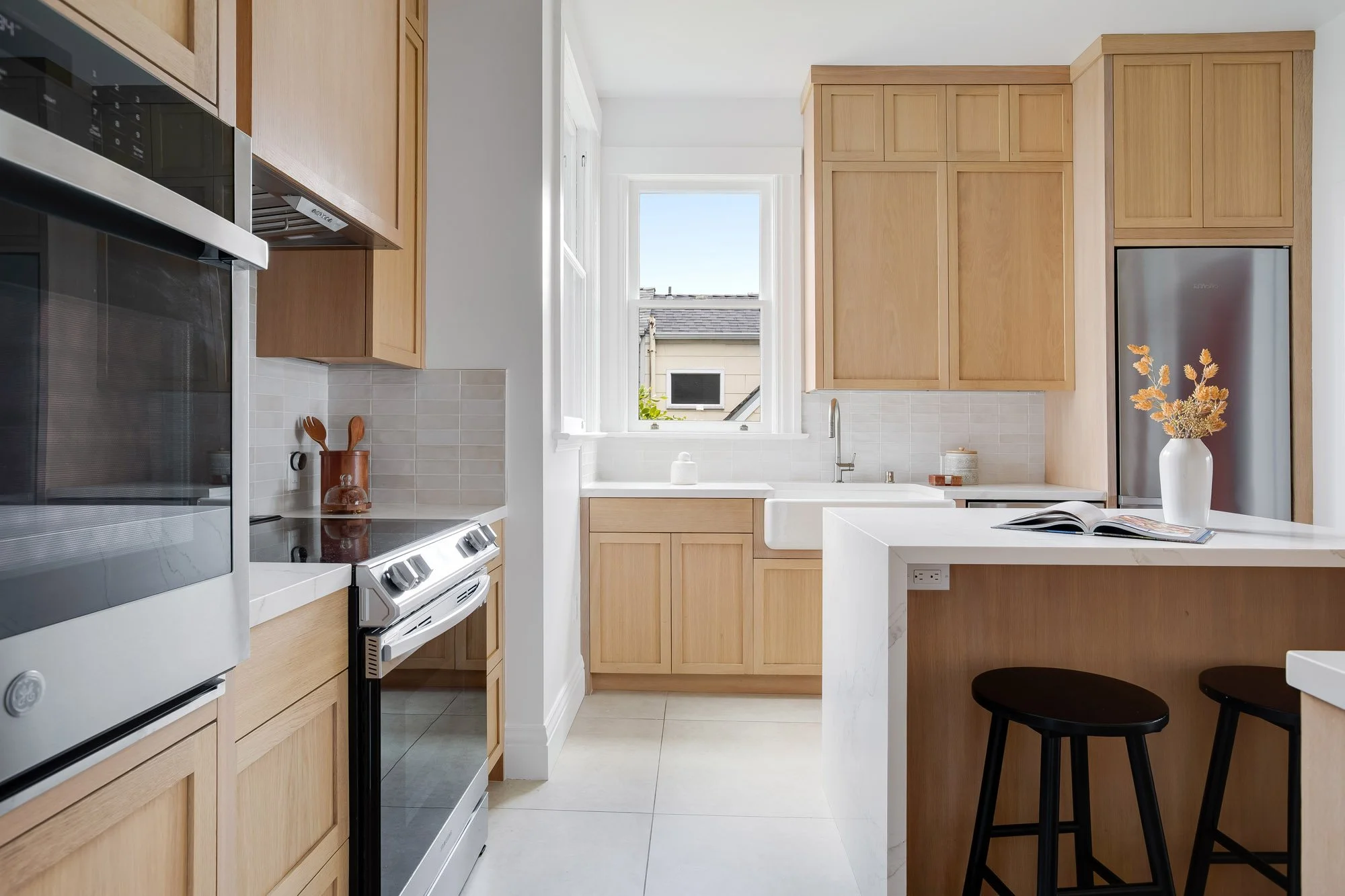 Renovated chef's kitchen with custom white oak shaker cabinetry, marble slab waterfall island, farmhouse sink, and large format tile floors in a Presidio Heights Victorian flat, San Francisco