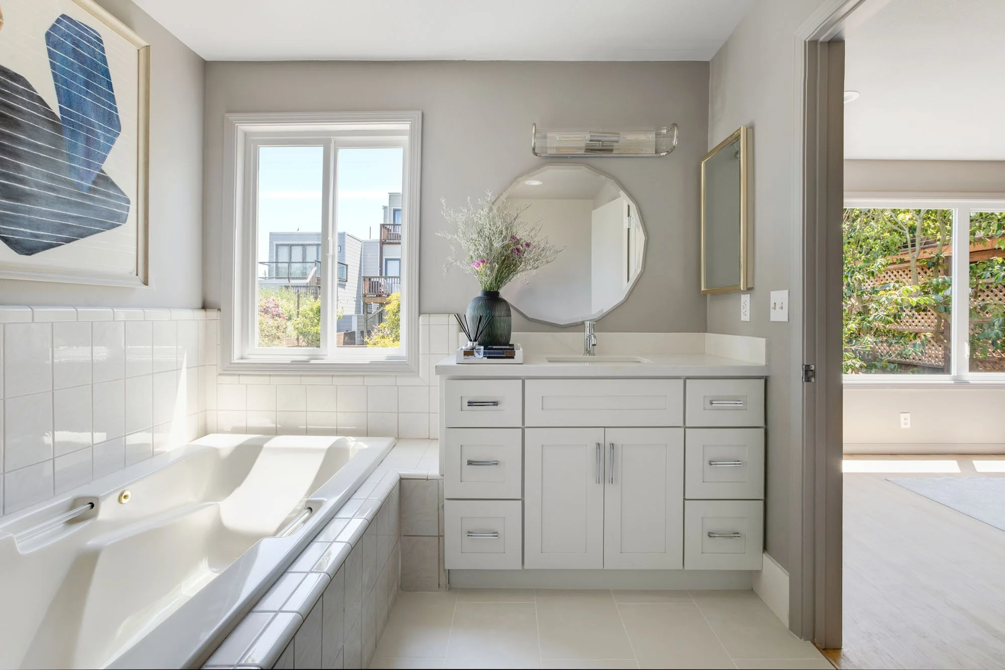 Renovated primary bathroom featuring a white shaker-style vanity, quartz countertops, a large soaking tub with white subway tile surround, and a scenic window view.