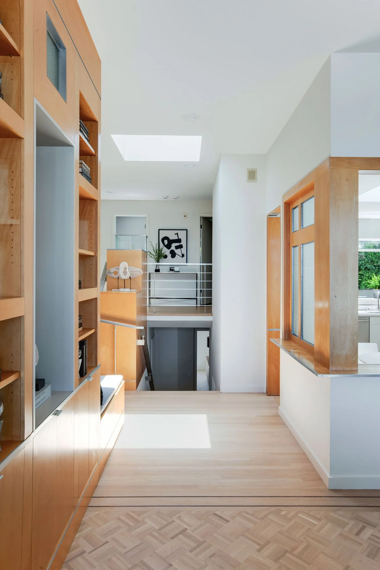 Architectural hallway view showing the transition between formal and informal living spaces, featuring a custom wood-framed pass-through to the kitchen and bright skylight.