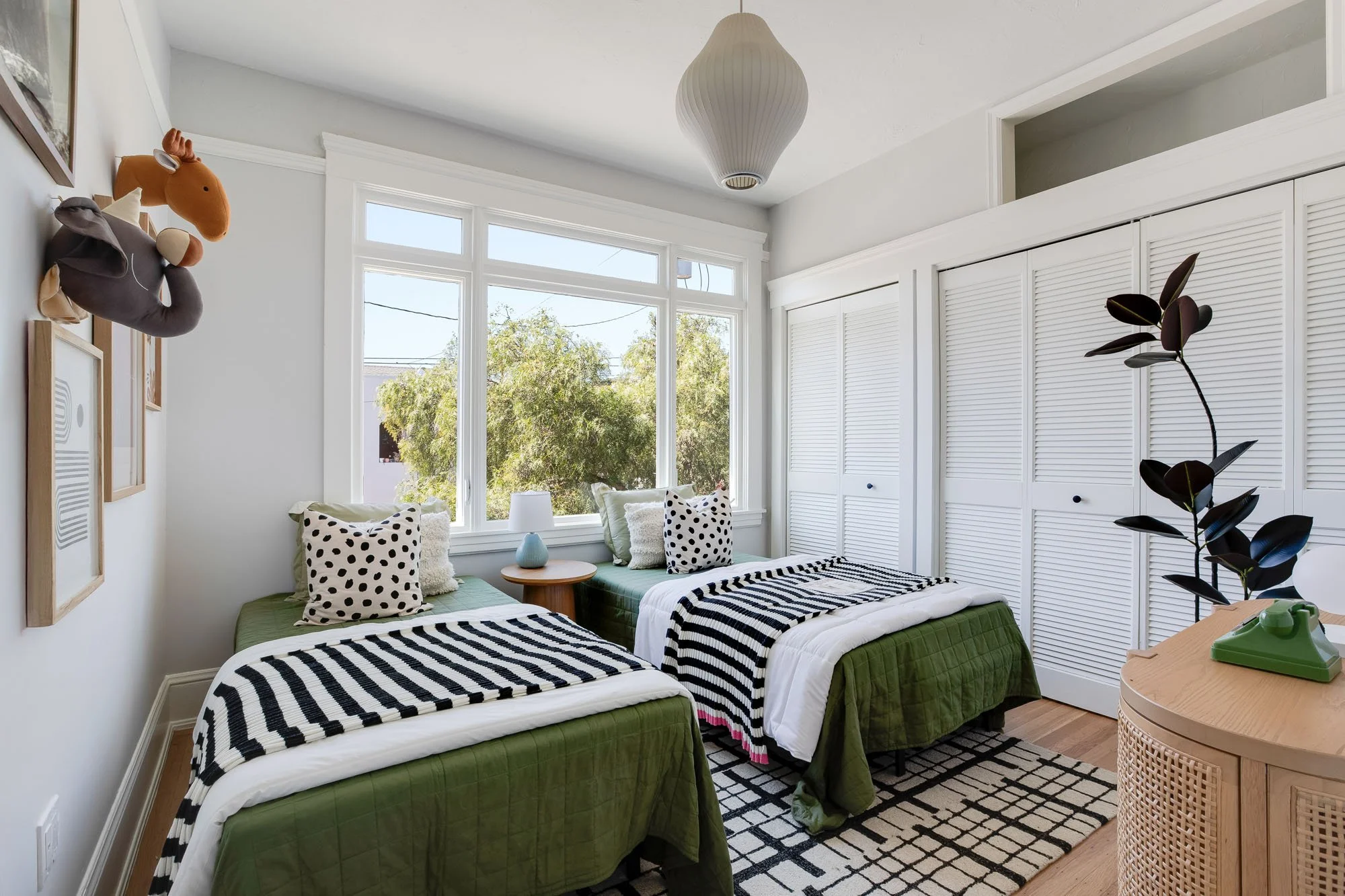 A bright children’s bedroom featuring twin beds with green linens, white louvered closet doors, and whimsical animal-head wall decor.