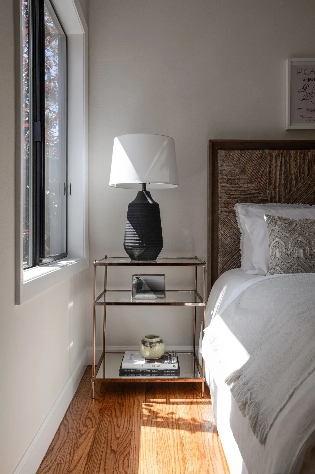 Close-up of a stylish bedroom nightstand featuring a black textured lamp and a tiered glass and metal side table.