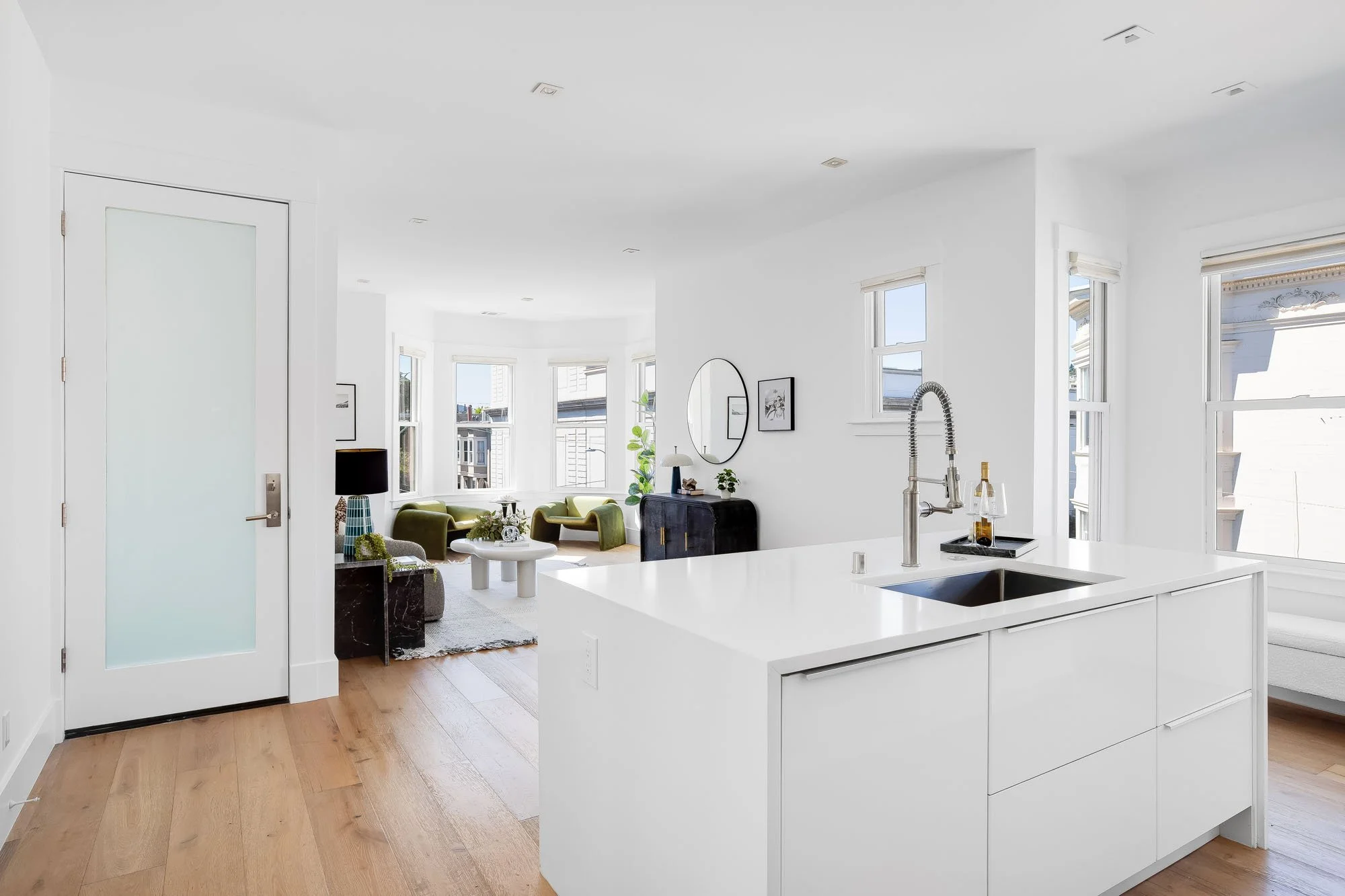 Open-concept kitchen and living area in a San Francisco luxury condo featuring minimalist white cabinetry and abundant natural light.