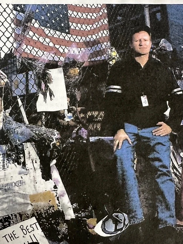 Peter J. Killeen standing at a September 11 memorial beside an American flag and tributes.