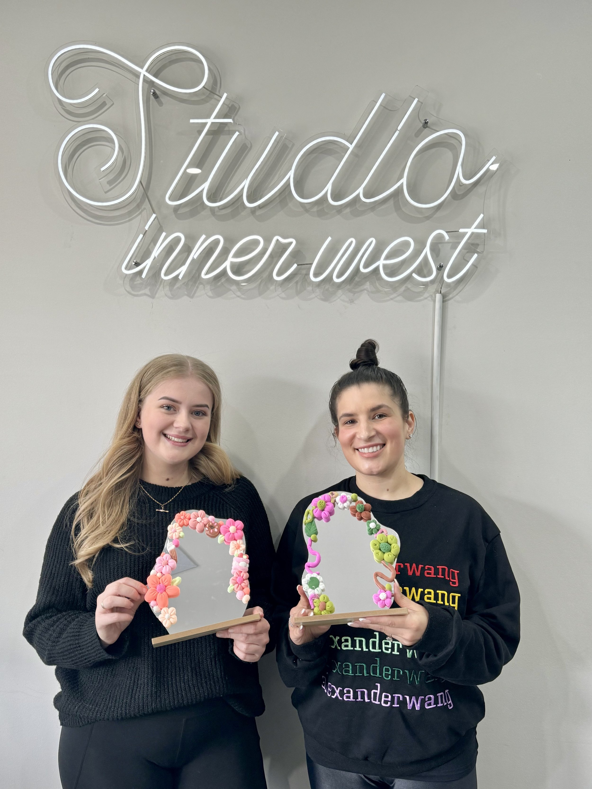 Two people holding decorative mirrors with a "Studio Inner West" sign in the background.