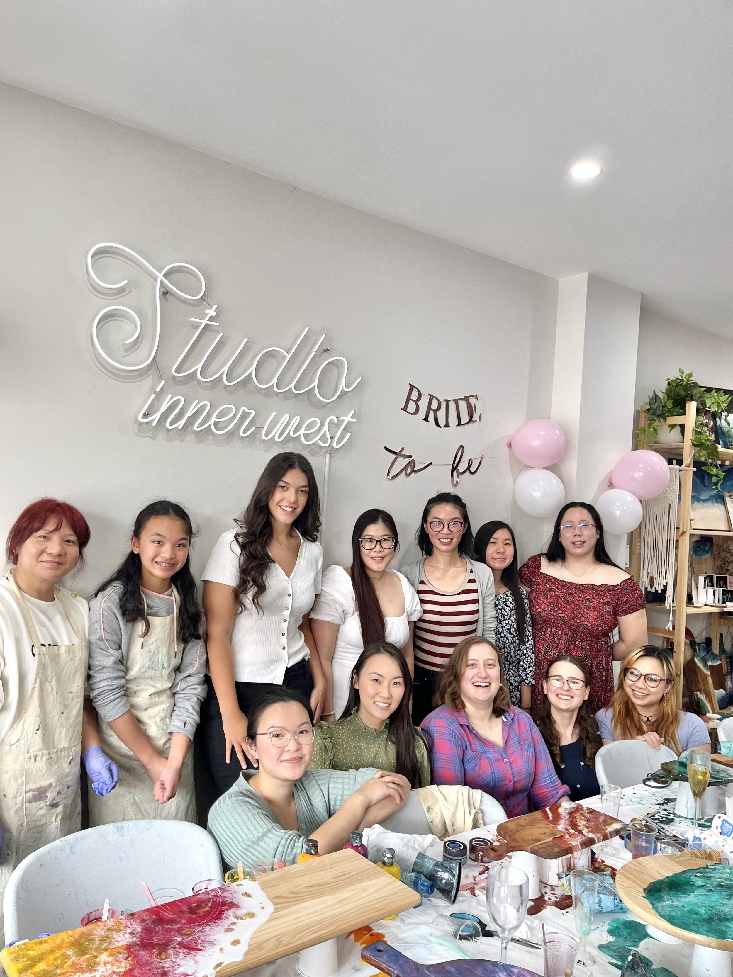Group of women at a bridal shower in a studio setting with art supplies and a "Bride to be" sign on the wall.