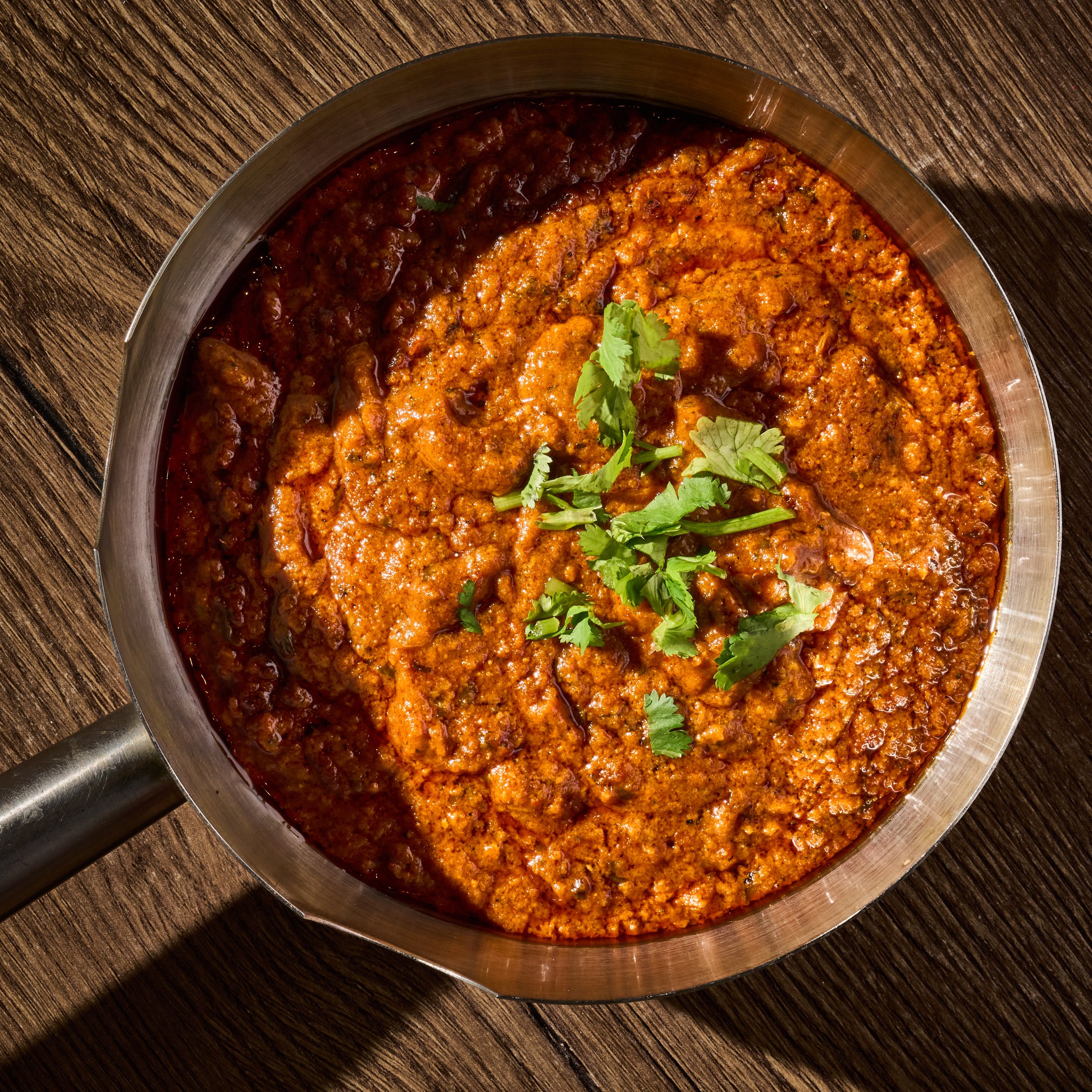 Pot of Indian curry with herbs on wooden table