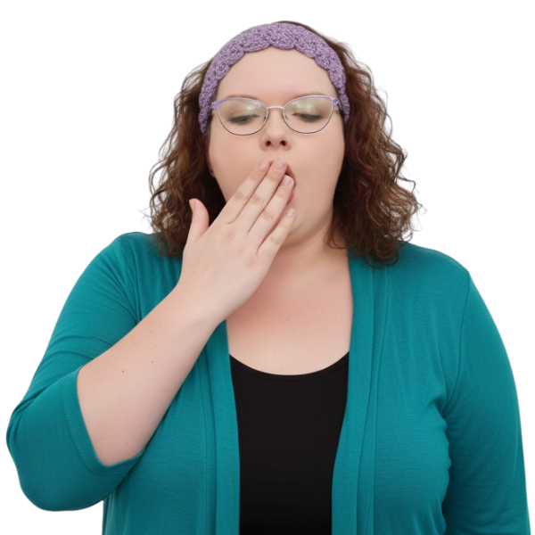A woman with curly brown hair, wearing glasses, a purple headband, and a teal cardigan, is yawning with her hand covering her mouth.