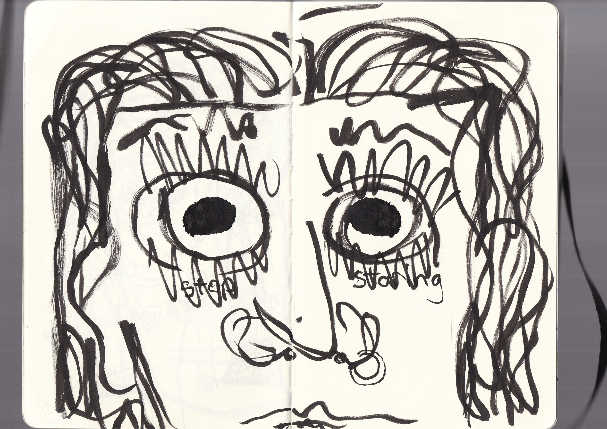 A black and white abstract drawing of two large faces with wide eyes and open mouths, made with bold, messy lines. The drawing is in a sketchbook with the pages laid flat, with the text 'still a' and 'STAY' visible below the faces.