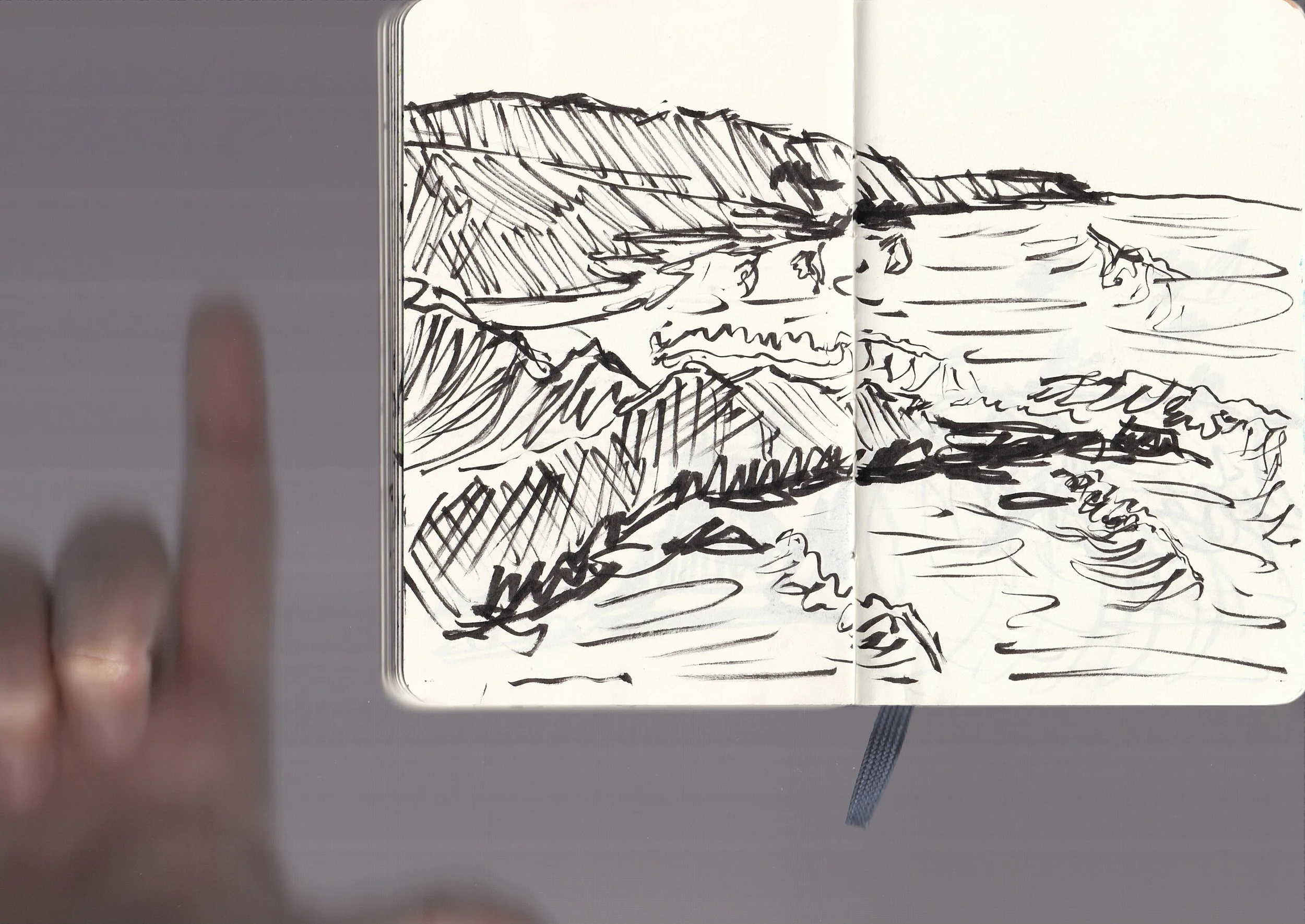 A black ink sketch of a coastal landscape with cliffs, water, and sky, drawn in a notebook.