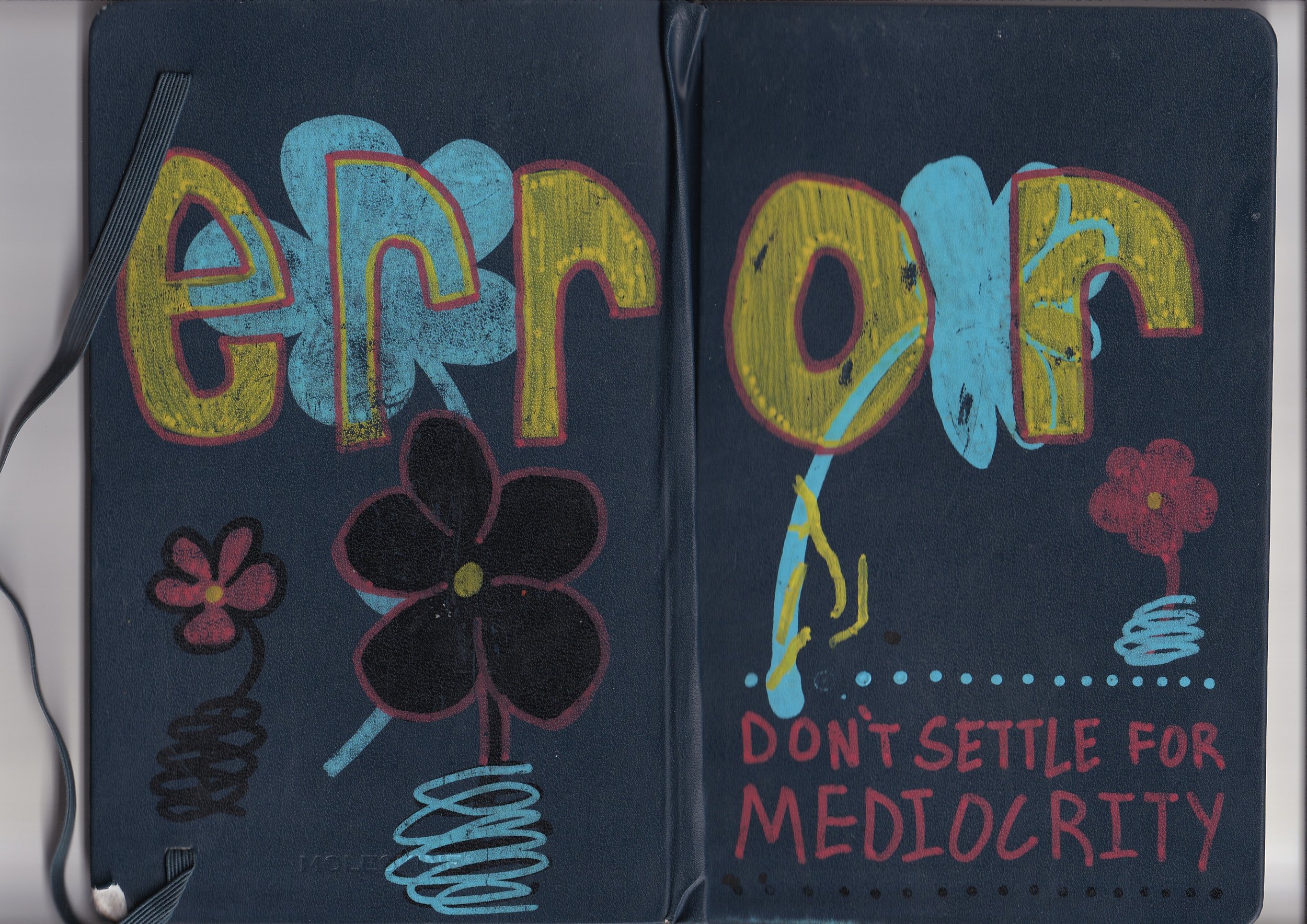 Close-up of a dark-colored notebook with bright, colorful graffiti-style artwork. The artwork features flowers, a lightning bolt, and various abstract shapes with a message in red text that reads 'DON'T SETTLE FOR MEDIOCRITY'.
