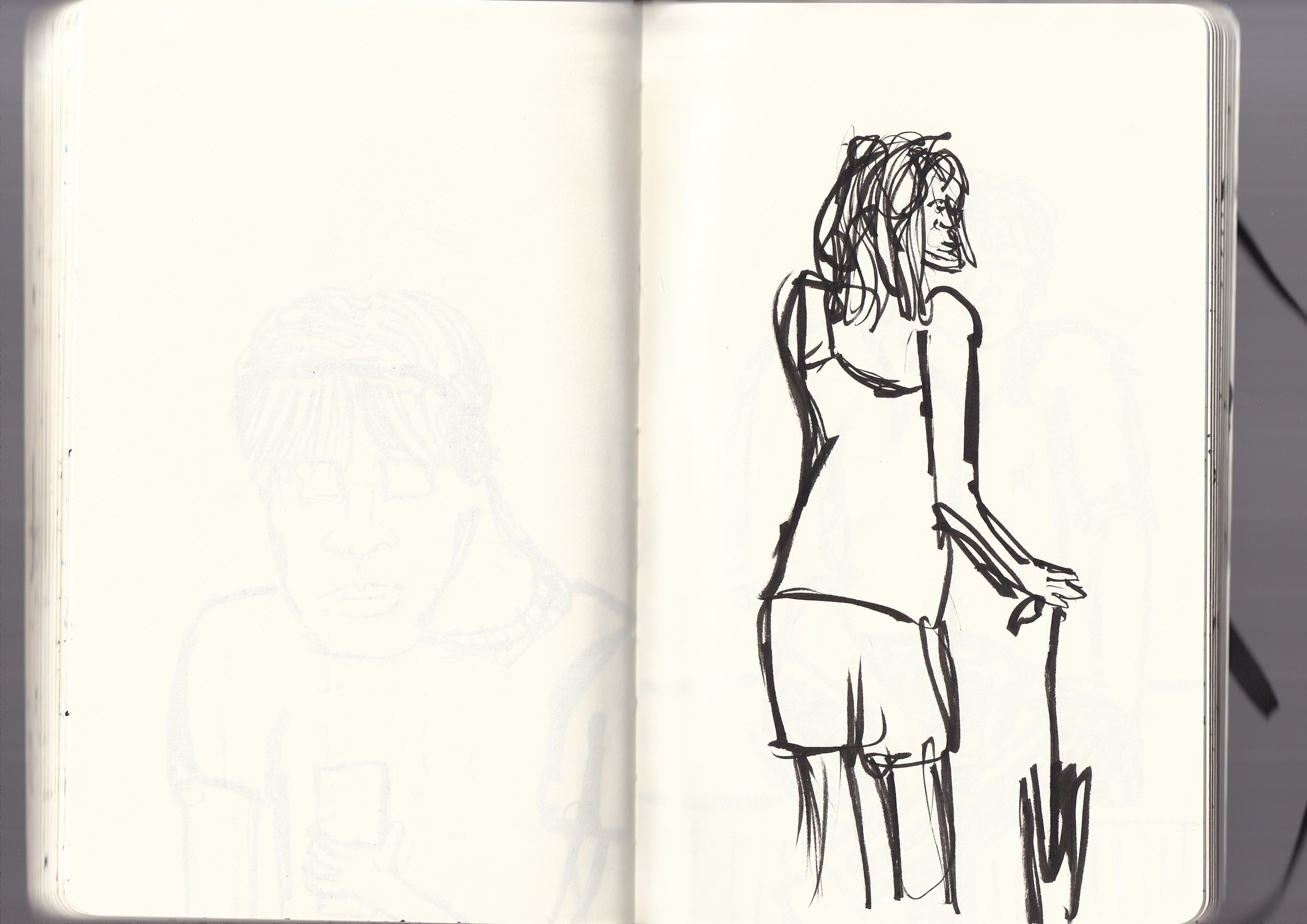 A black ink sketch of a woman with long hair, wearing a dress, and standing with one hand on her hip, on an open white sketchbook.